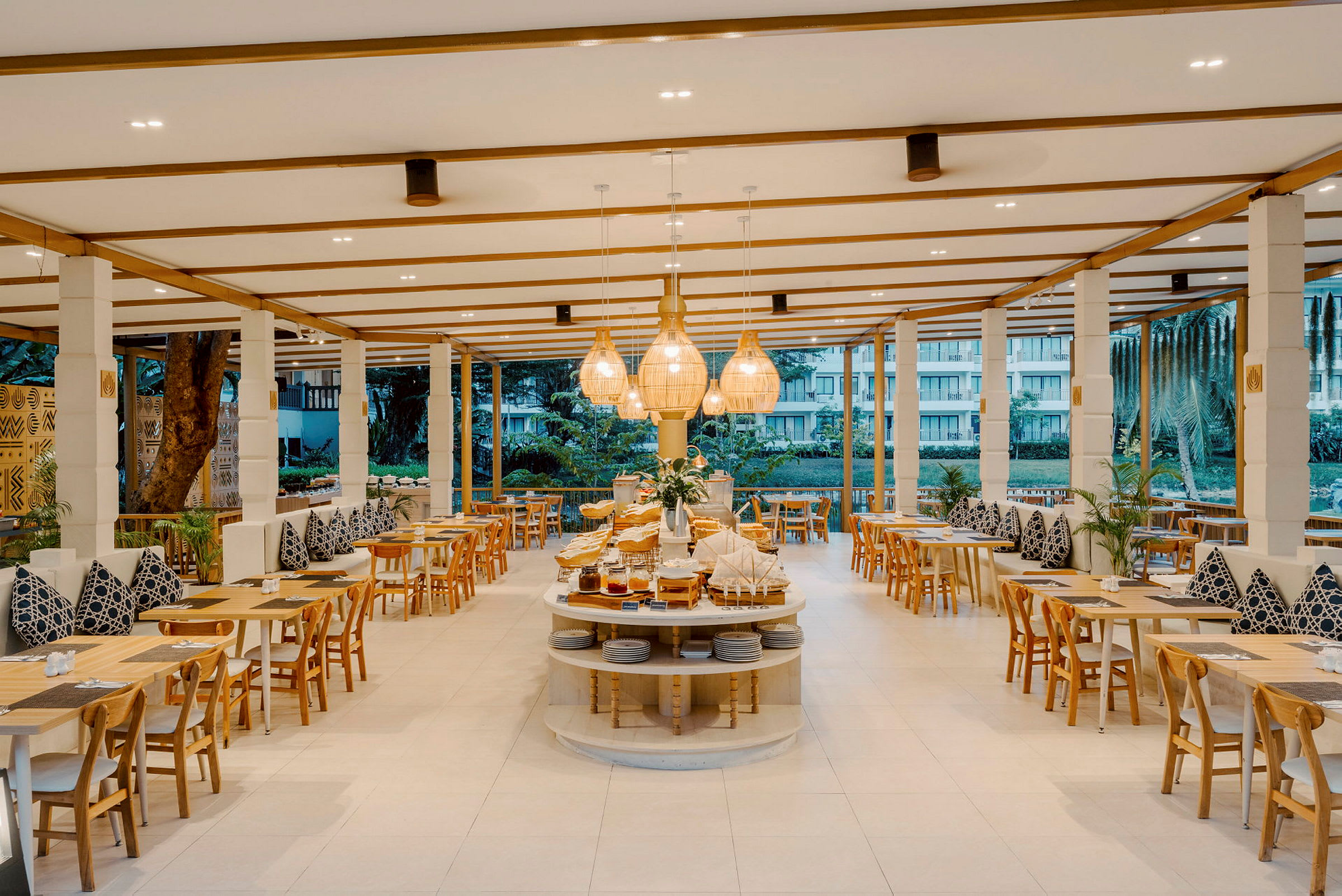 En moderne og lys restaurant med tremøbler og dekorerte puter på benker. Sentralen er et buffetbord med mat og lamper over. (AI-generert tekst)