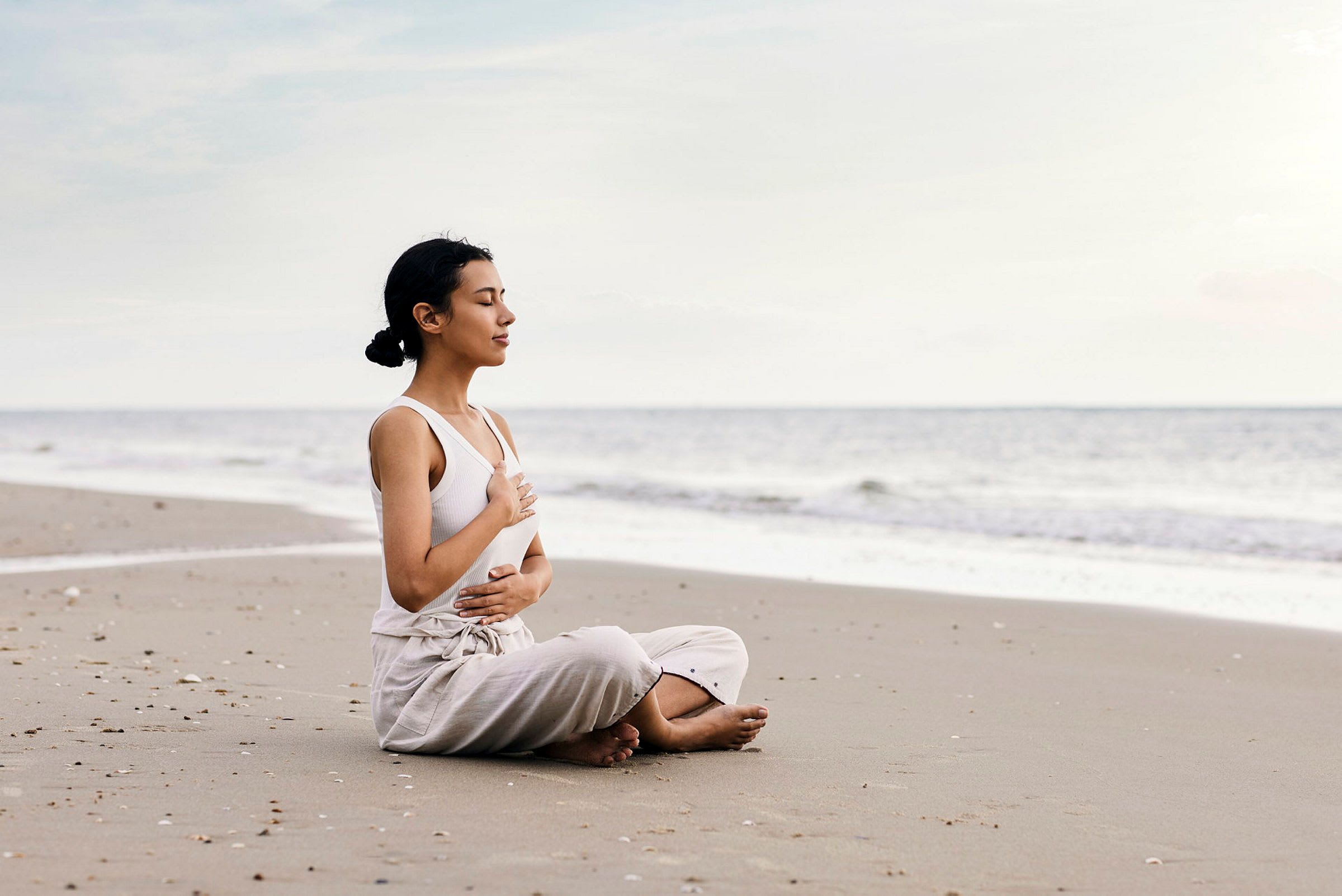 Person sitter på en strand og holder hånden på brystet. (AI-generert tekst)