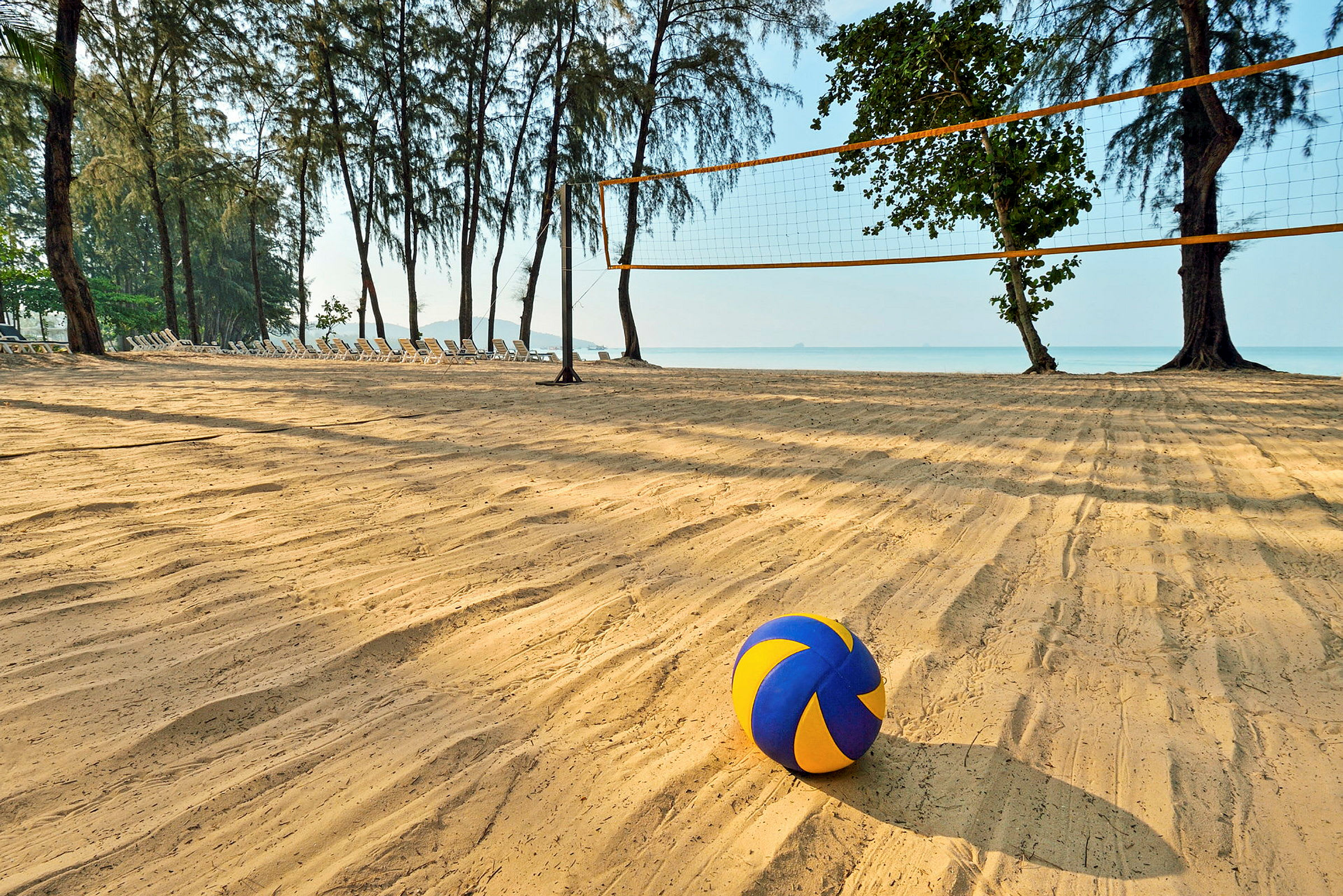 En strand med et volleyballnett og en fargerik volleyball i forgrunnen. (AI-generert tekst)