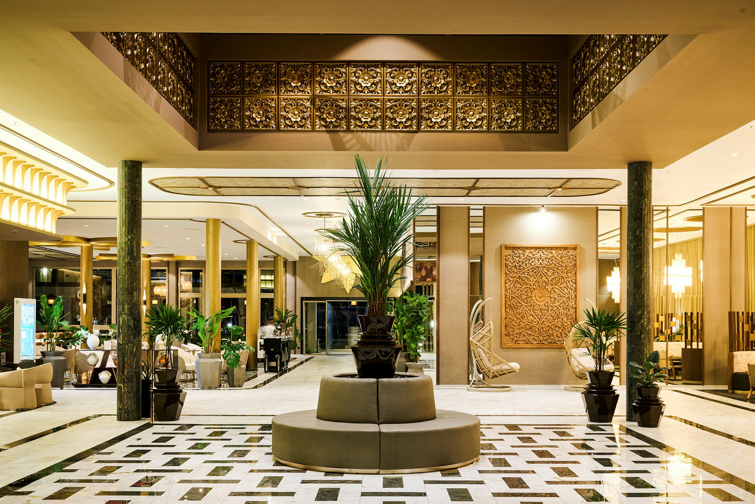 En elegant hotellobby med marmorgulv, dekorasjoner i gull og tre, og planter plassert rundt området. (AI-generert tekst)