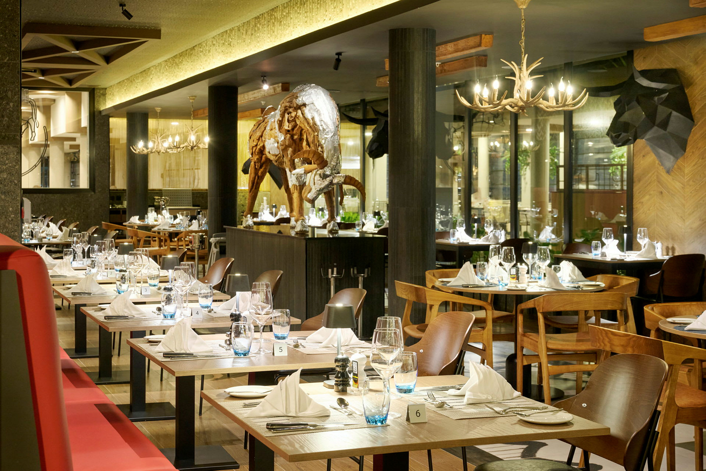 En elegant restaurant med dekkede bord og en skulptur av en bøffel i midten av rommet. (AI-generert tekst)