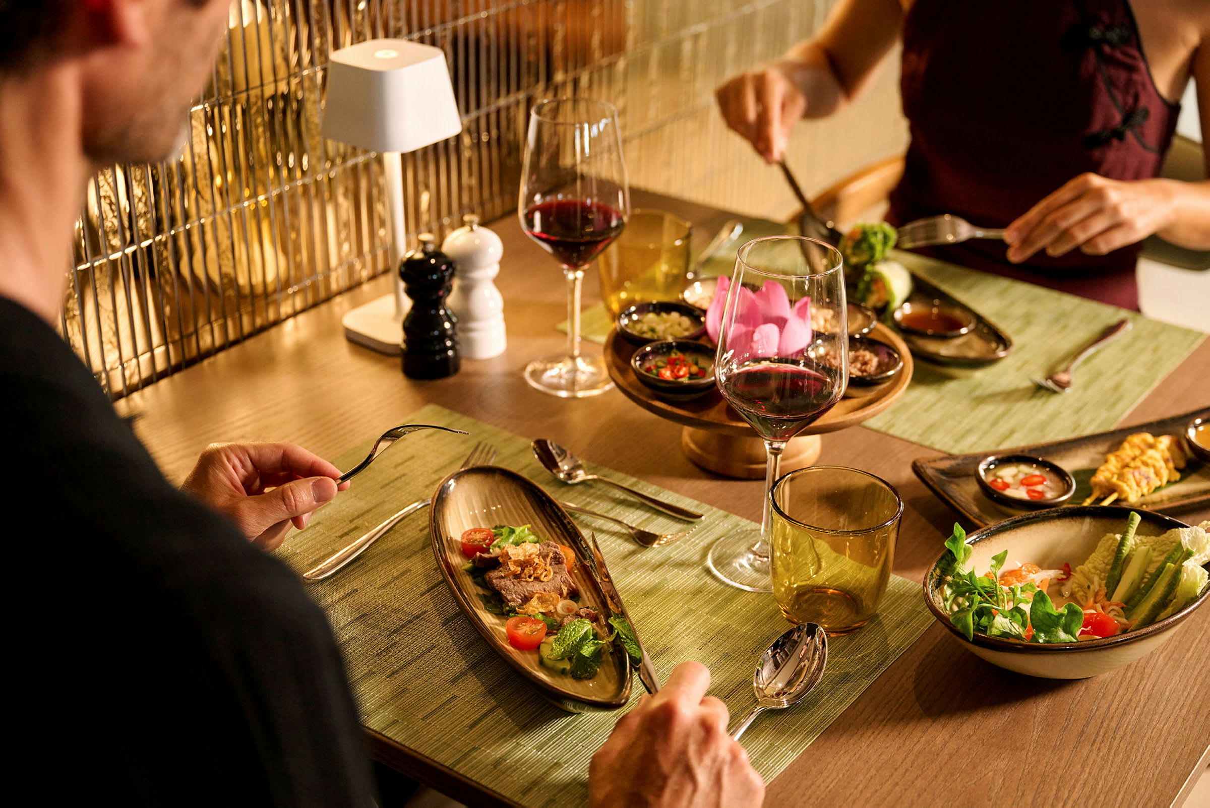 To personer sitter ved et bord med elegante tallerkener og vinglass, omgitt av smakfullt oppsatte retter. (AI-generert tekst)