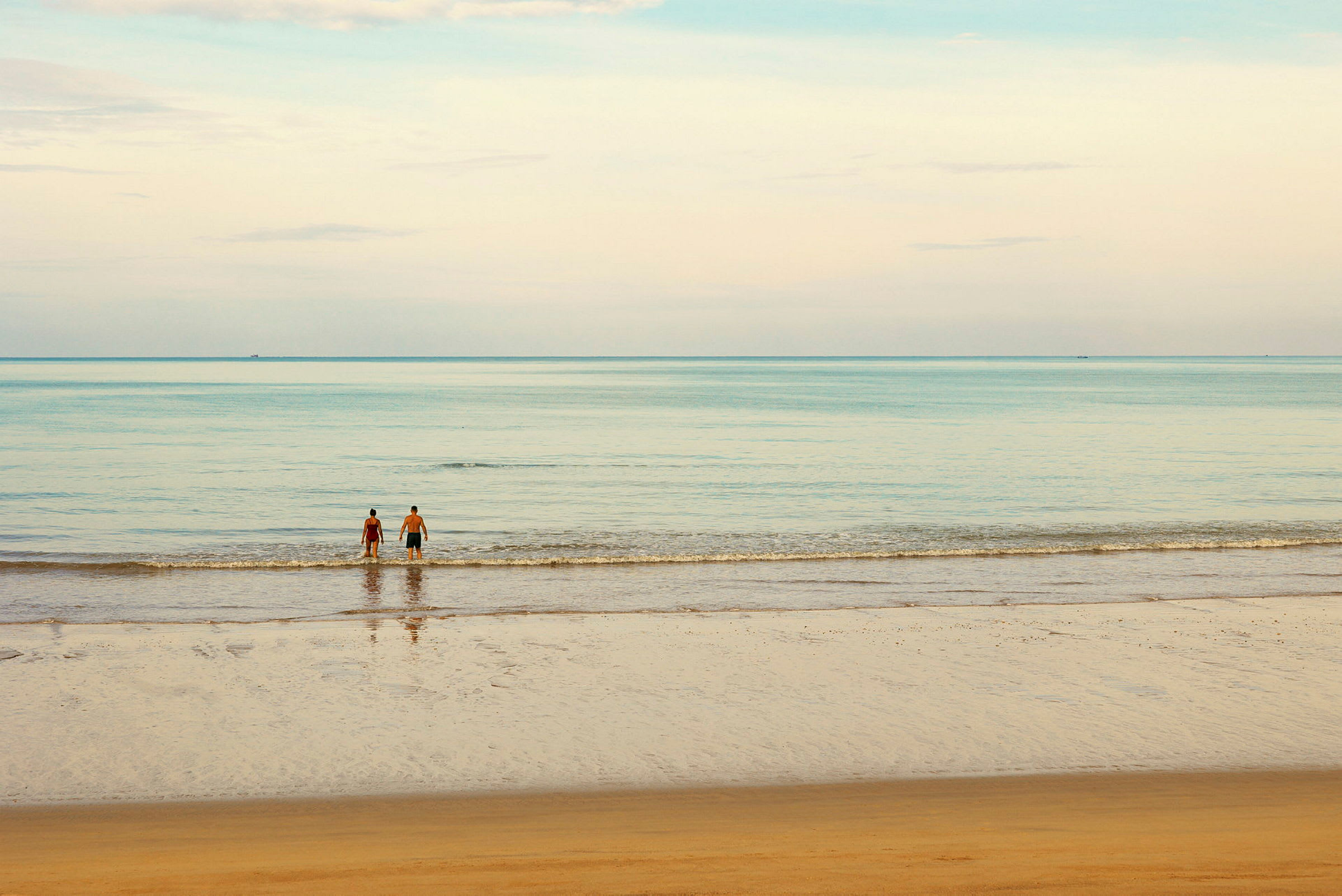 En strand med to personer som står ved vannkanten og ser utover havet. (AI-generert tekst)