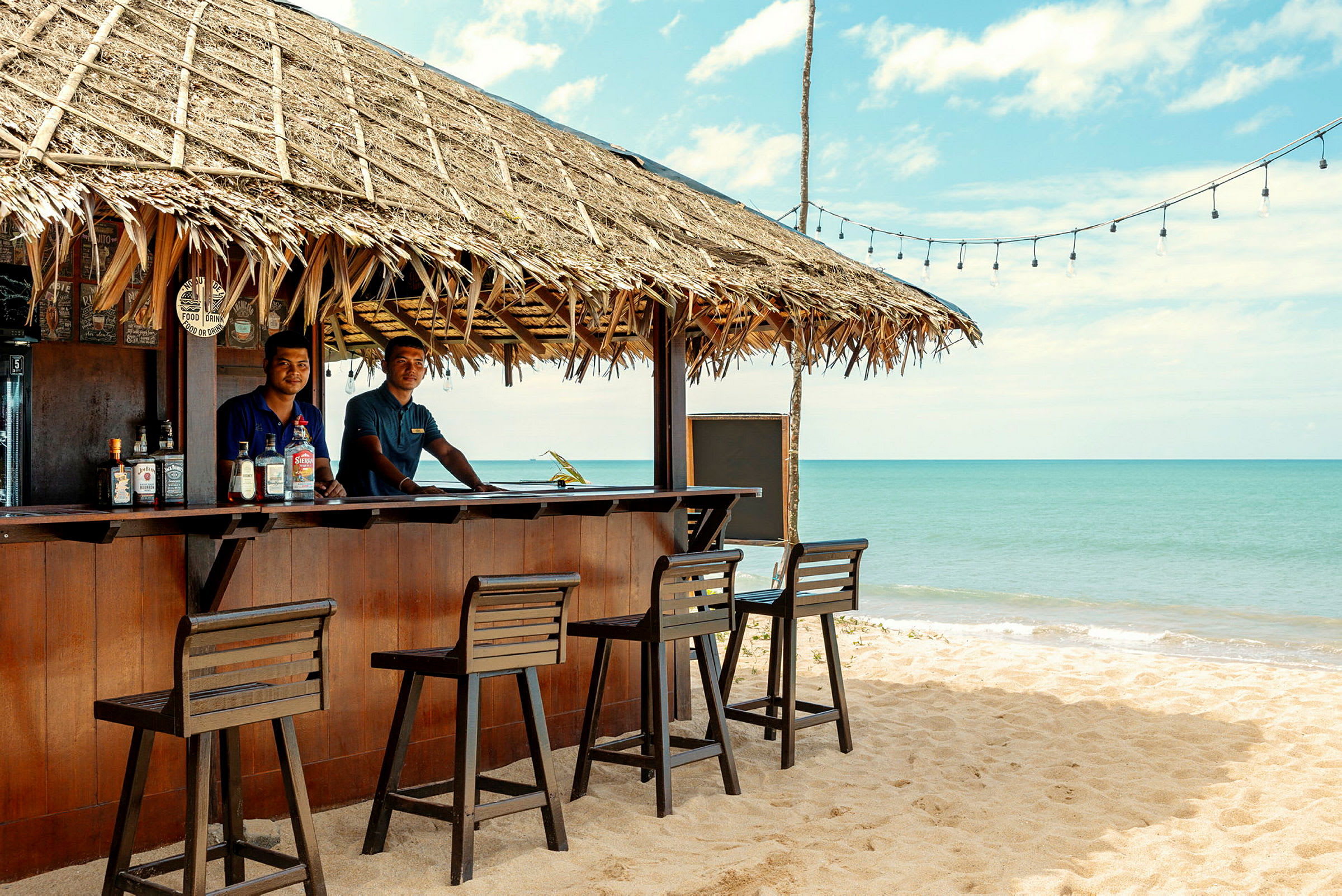 Strandbar med stråtakt og havet i bakgrunnen. (AI-generert tekst)