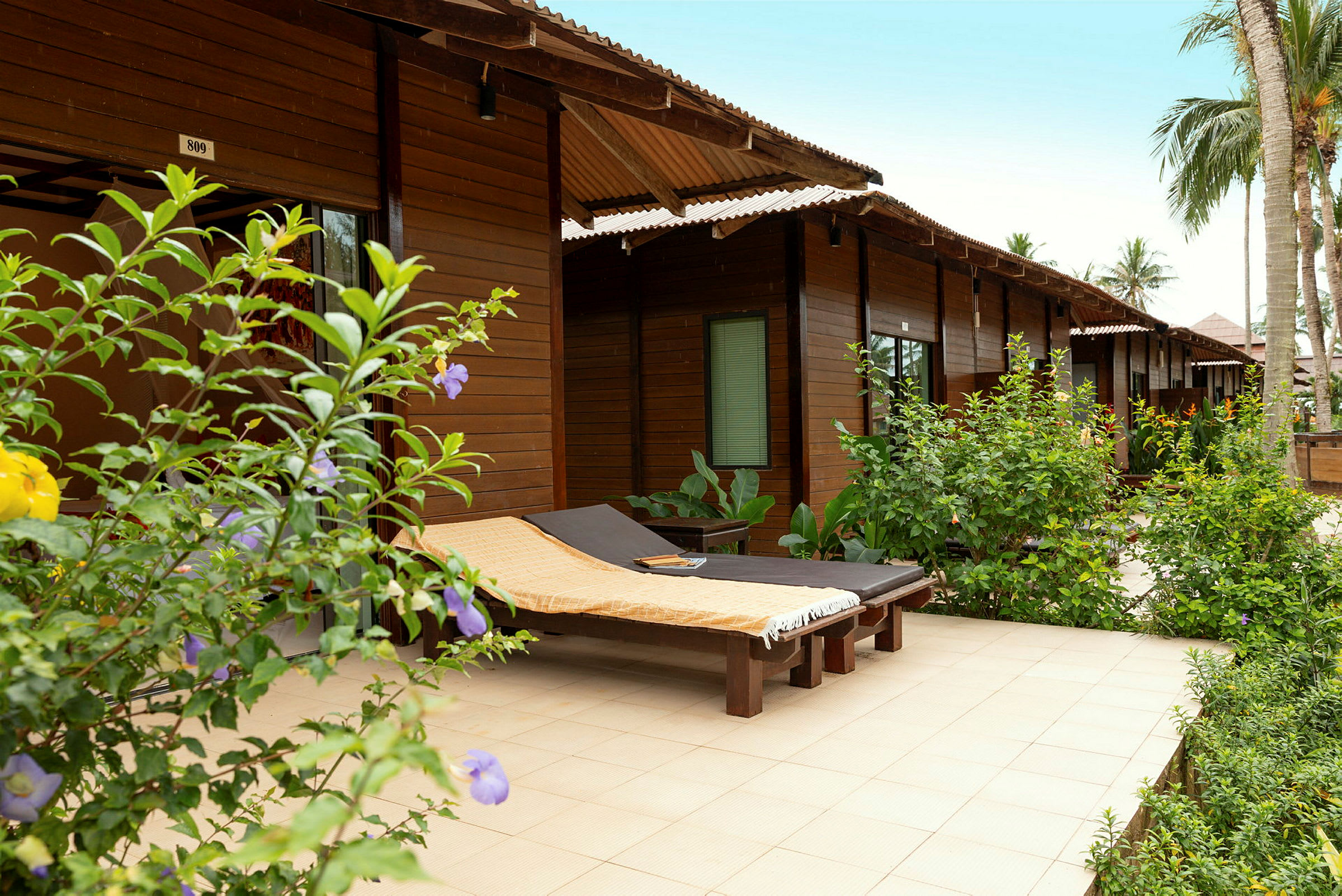 Treterrasse med solsenger omgitt av grøntområder ved en rekke trebungalower. (AI-generert tekst)