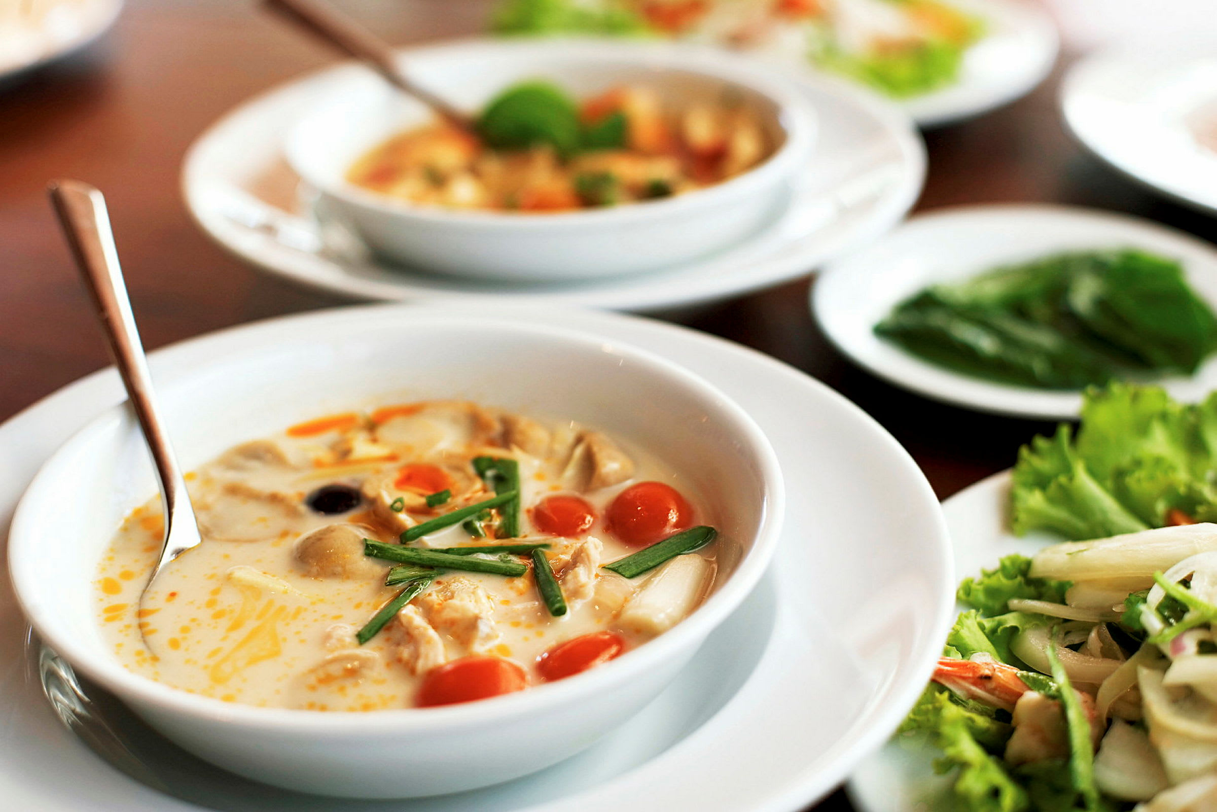 Hvit bolle med suppe, som inneholder grønnsaker og urter, på et bord. (AI-generert tekst)