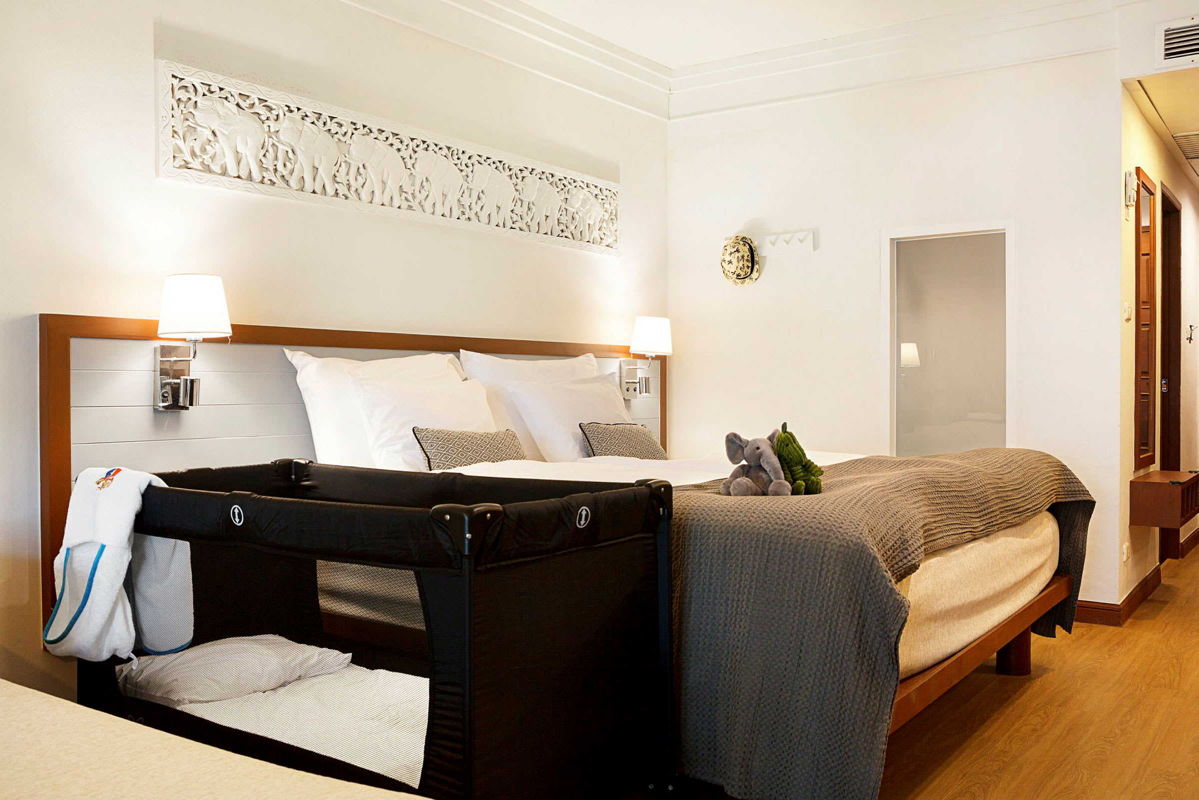 Hotellrom med en dobbeltseng, en barneseng og to kosedyr på sengen. (AI-generert tekst)