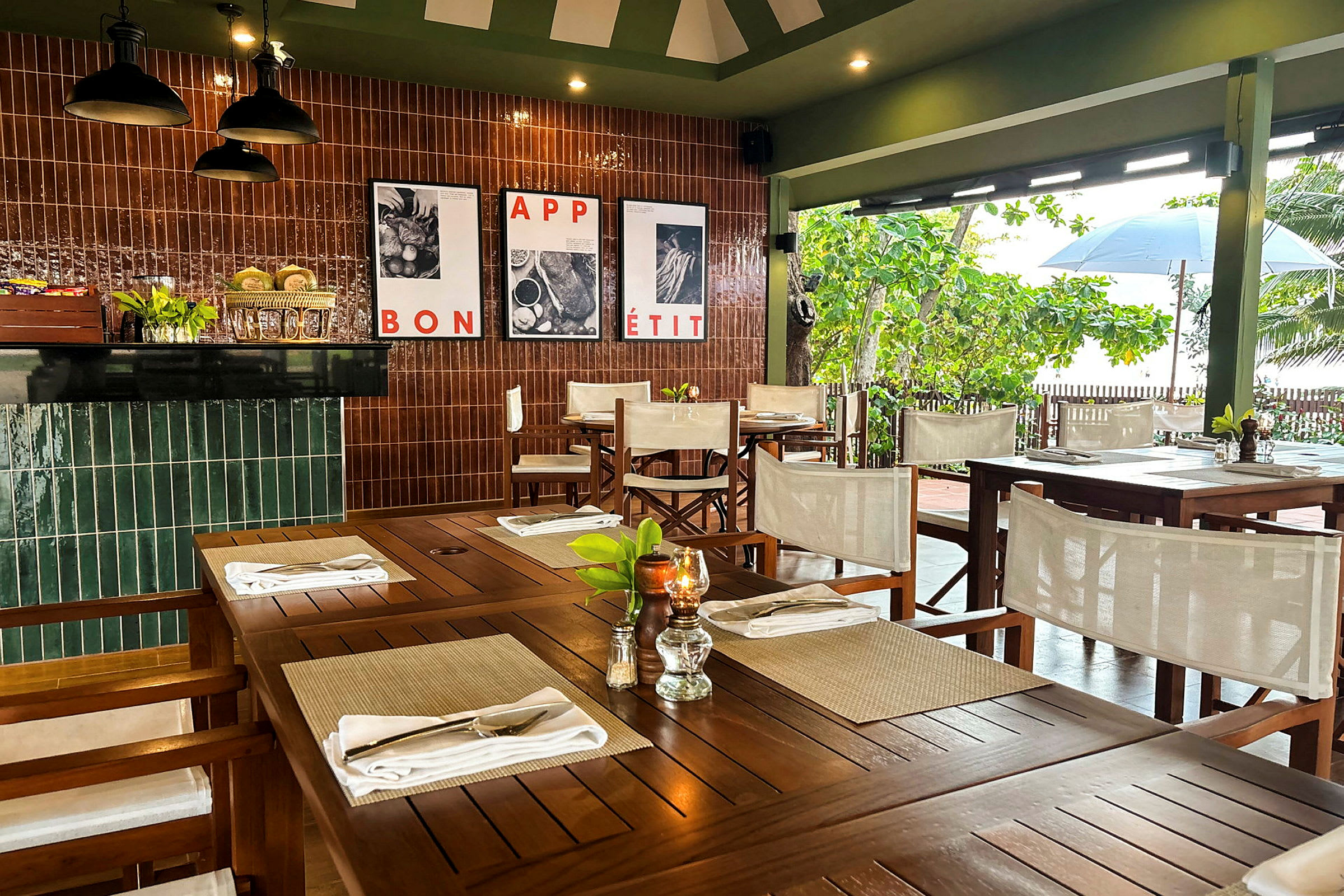 Interiør av en restaurant med tremøbler og dekkede bord, omgitt av grønne vegger og vinduer med utsikt mot vegetasjon. (AI-generert tekst)