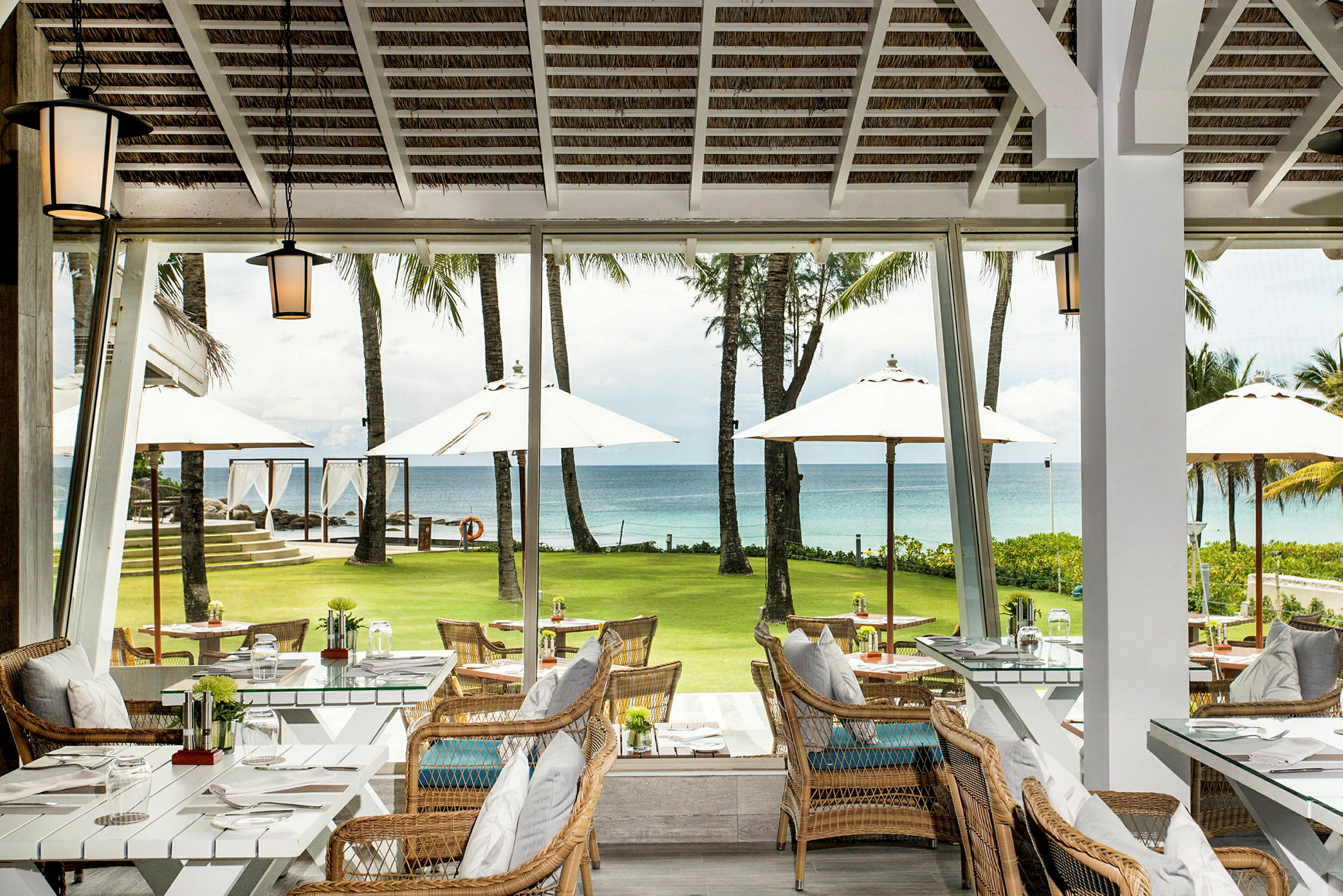 Restaurant med sitteplasser og utsikt over en grønn plen, parasoller og havet. (AI-generert tekst)
