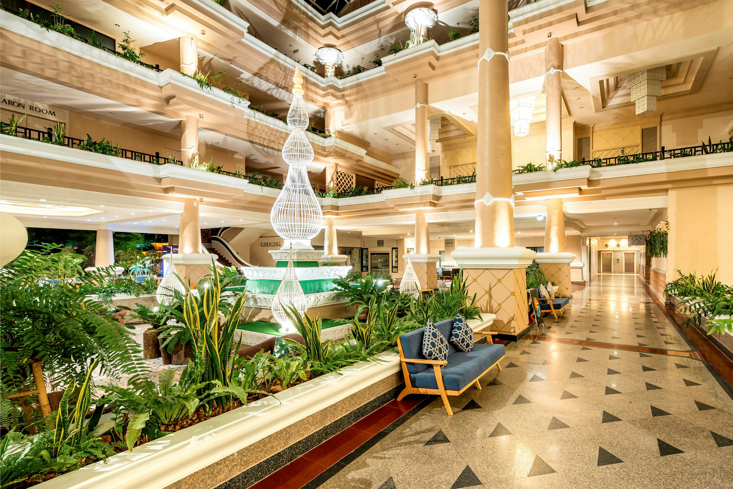 En lys og elegant hotellobby med søyler, frodige planter og dekorativ belysning. (AI-generert tekst)