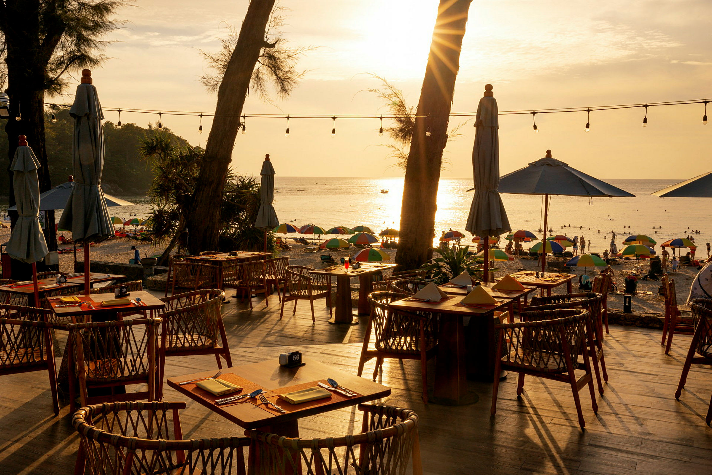 Restaurant ved stranden med uteservering, utsikt mot havet og solnedgangen. (AI-generert tekst)