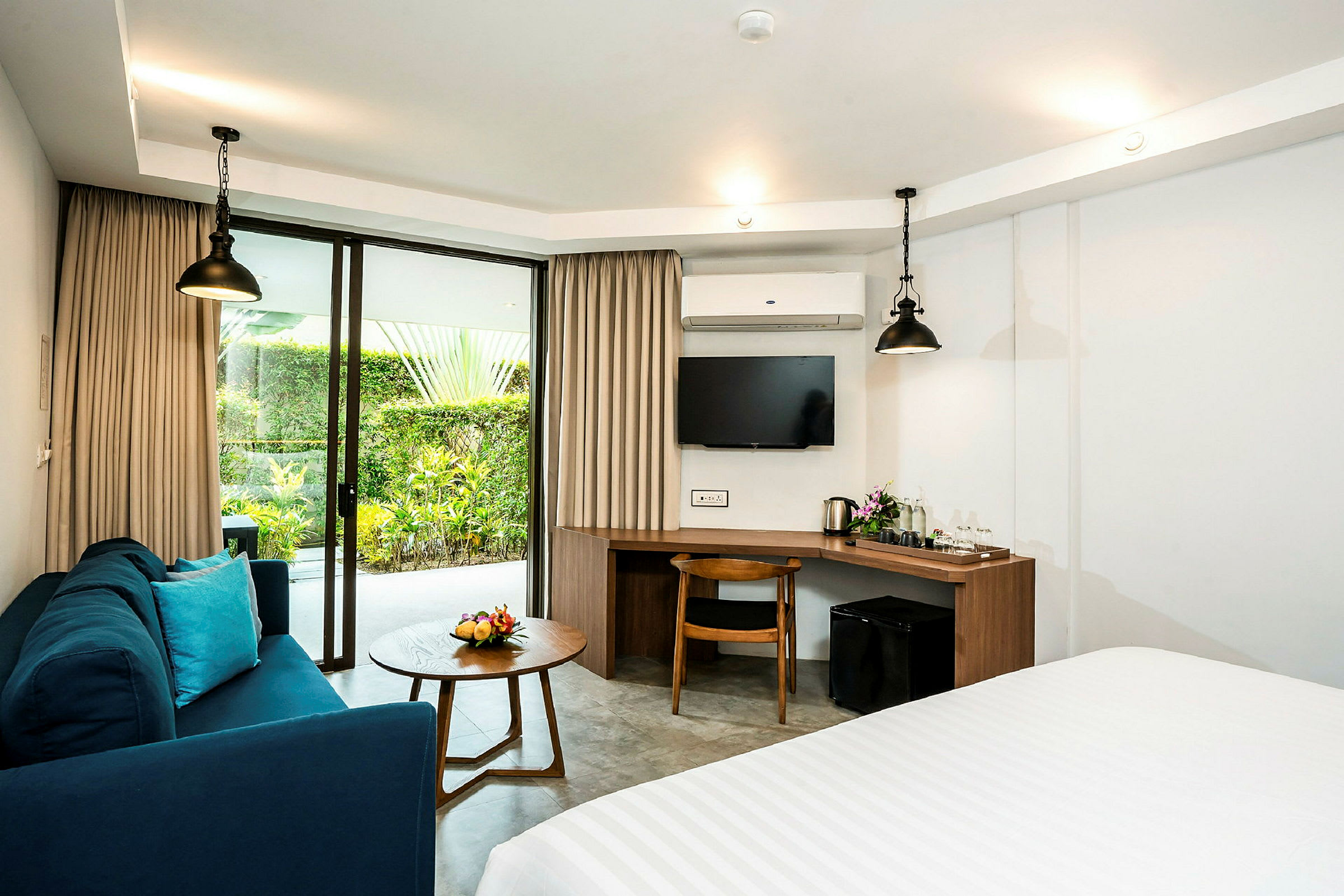 Et hotellrom med sofa, bord, skrivebord, TV og glassdører mot en hage. (AI-generert tekst)