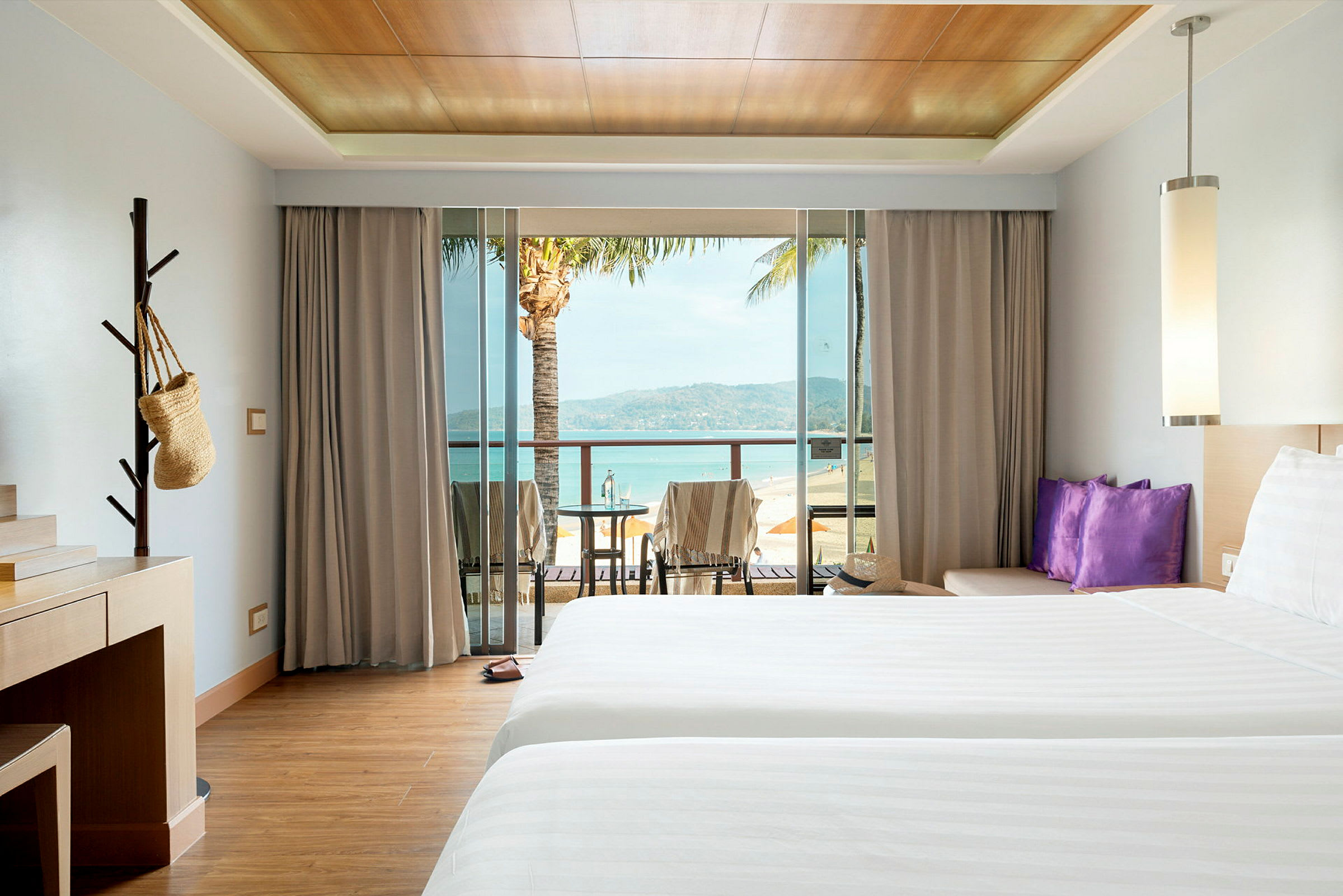 Hotellrom med to senger, skrivebord og balkong med utsikt over stranden. (AI-generert tekst)