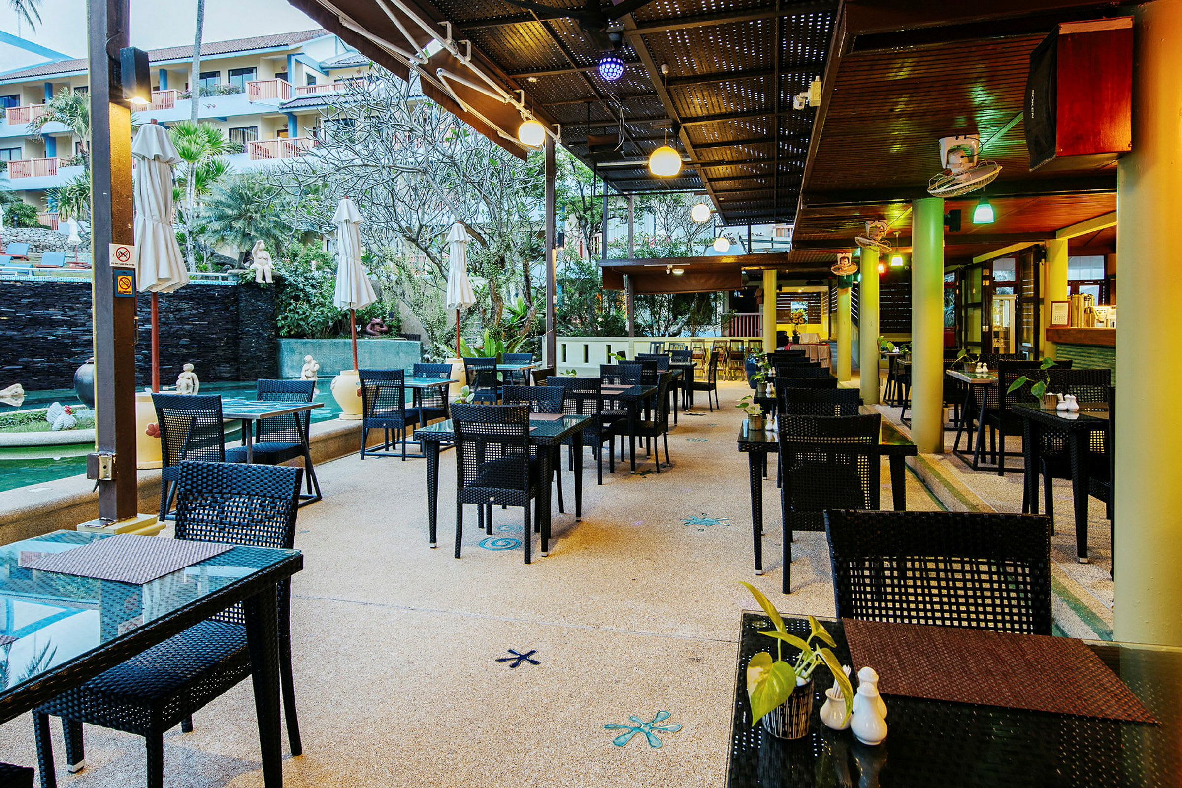 Bilde av en utendørsrestaurant med bord og stoler under en overbygning. (AI-generert tekst)