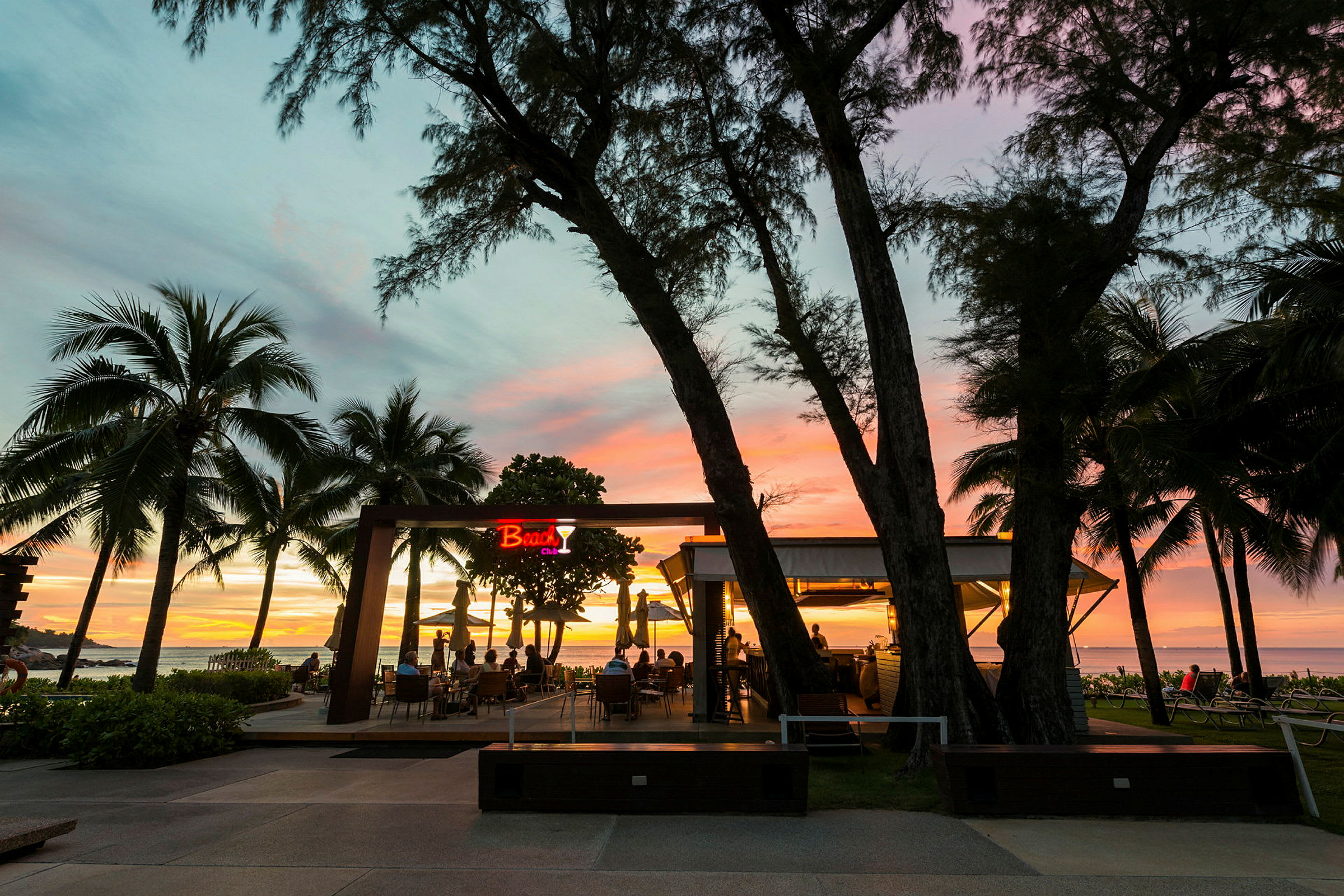 En strandbar med utsikt mot havet ved solnedgang, omgitt av palmer. (AI-generert tekst)