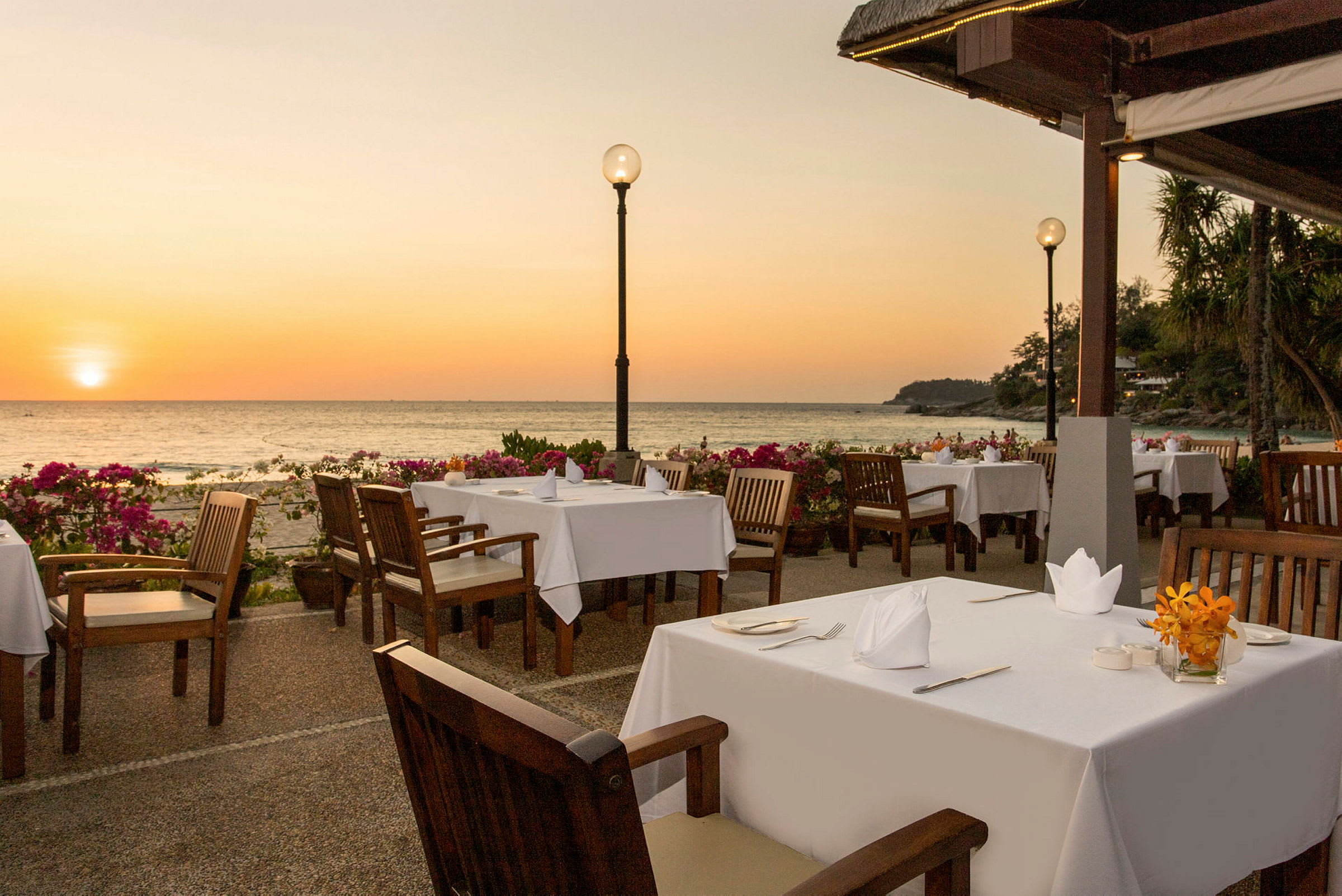 Utendørs restaurant med dekkede bord nær havet ved solnedgangen. (AI-generert tekst)