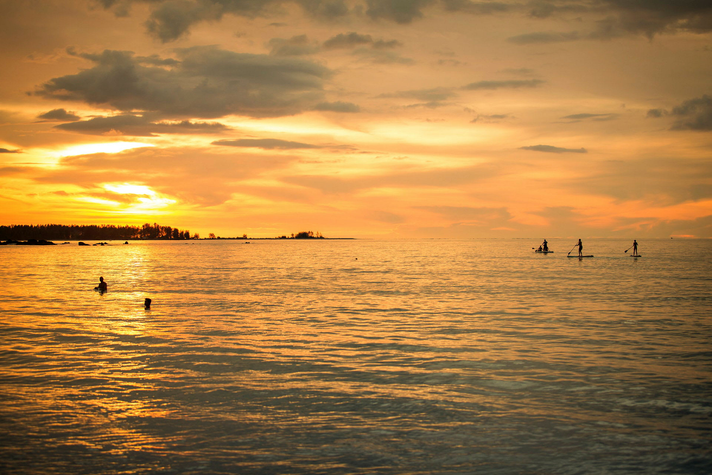 Personer som padler på paddleboards i havet under solnedgang, mens noen andre svømmer i nærheten. (AI-generert tekst)