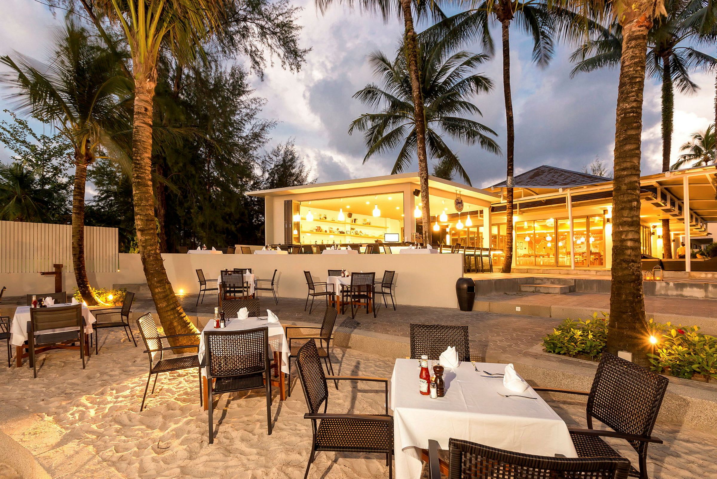 Restaurant med uteservering ved stranden, omgitt av palmetrær. (AI-generert tekst)