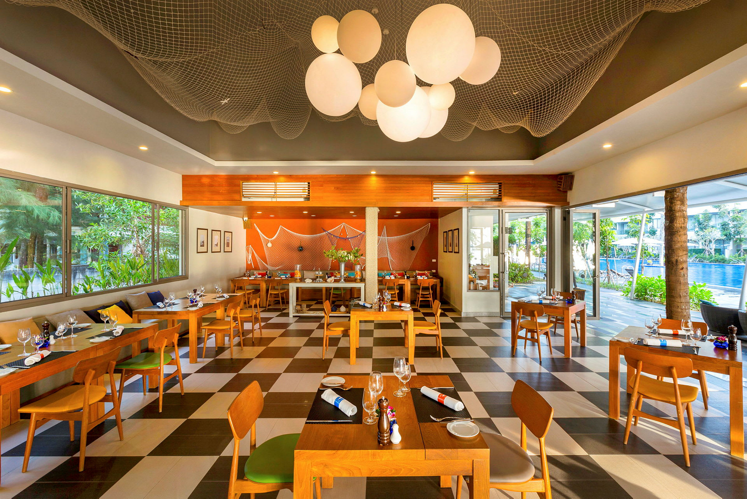 Restaurant med trebord og stoler samt store vinduer med utsikt over grøntområder og et basseng utenfor. (AI-generert tekst)