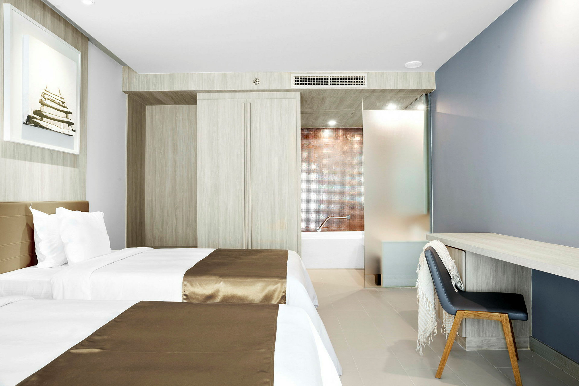 Hotellrom med to enkeltsenger, skrivebord og stol, samt utsikt mot badet. (AI-generert tekst)