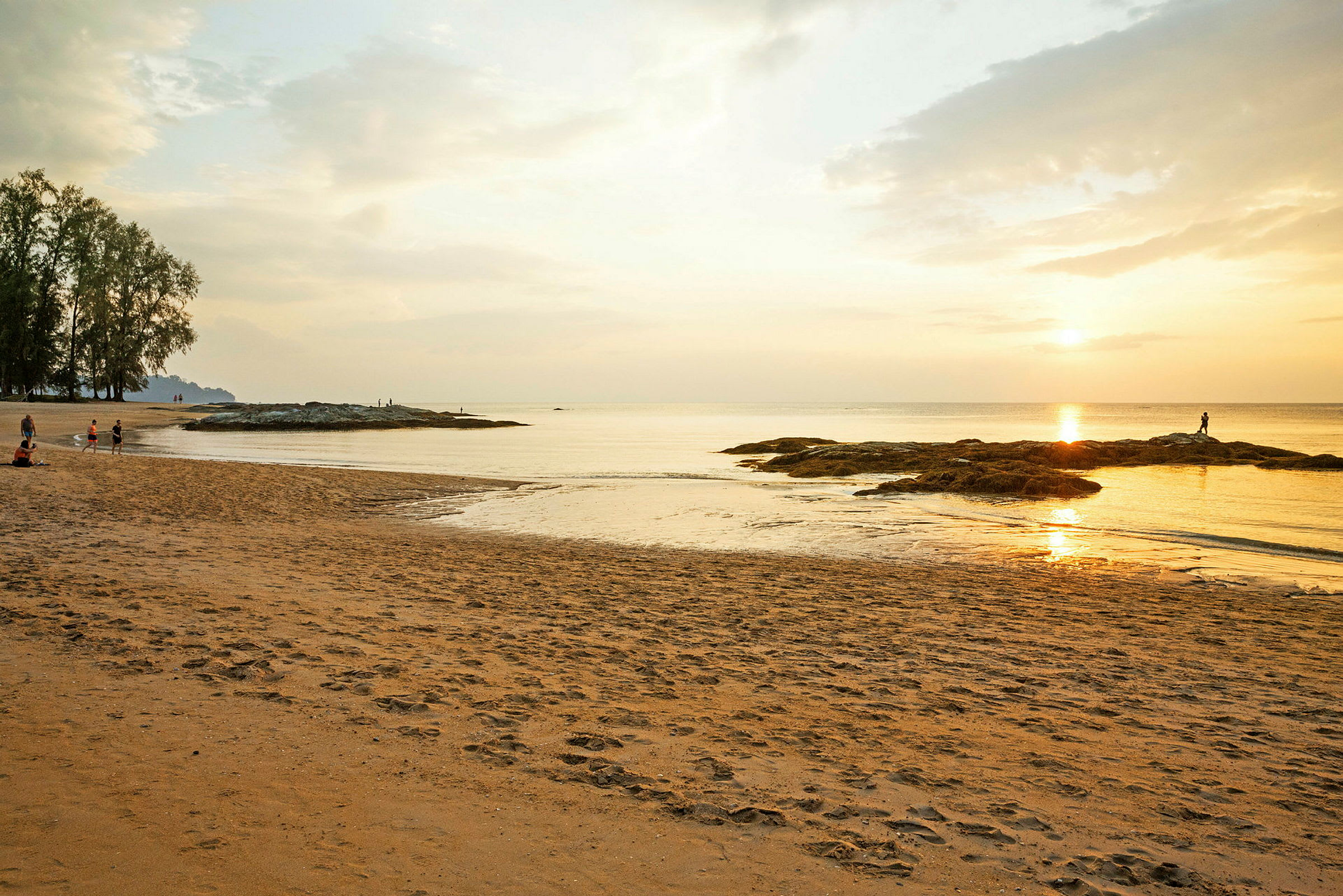 Solnedgang ved en rolig strand med noen mennesker og steiner ved vannet. (AI-generert tekst)