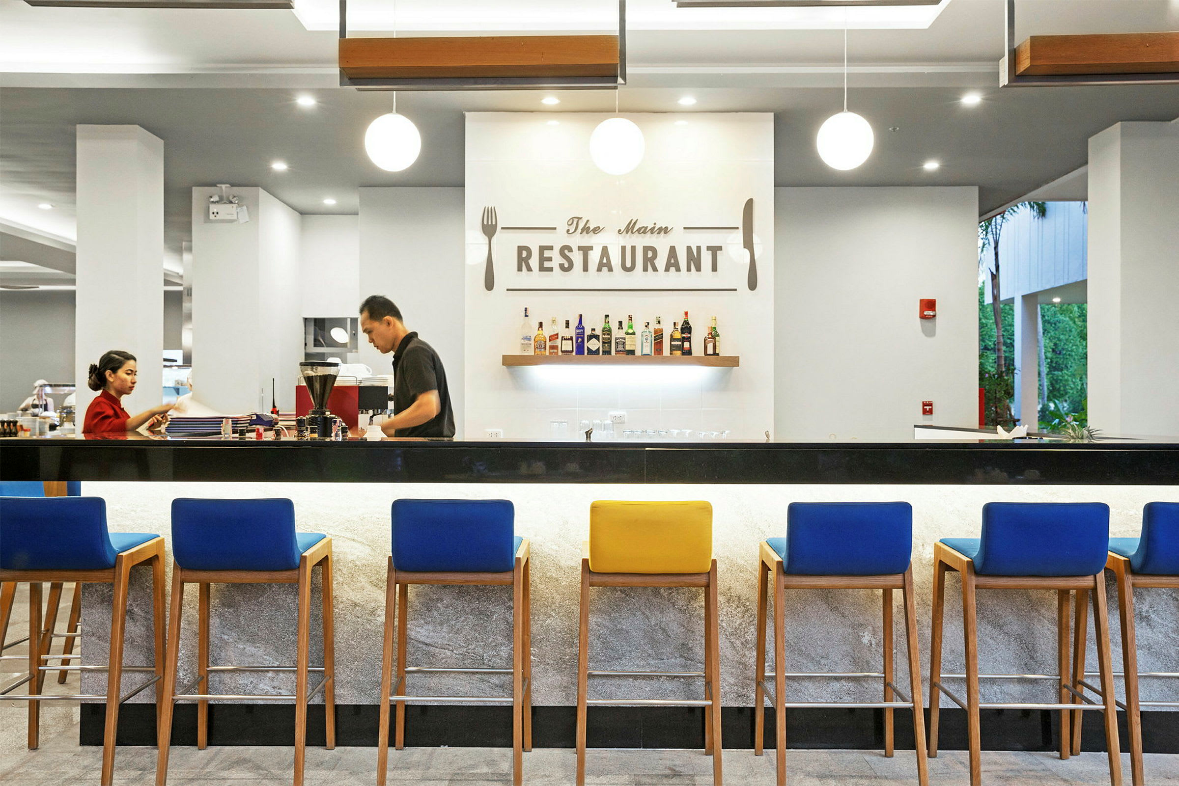 En elegant restaurant med moderne innredning, en bar med fargerike stoler og en vegg med opphengte flasker og et skilt med teksten 'The Main Restaurant'. (AI-generert tekst)