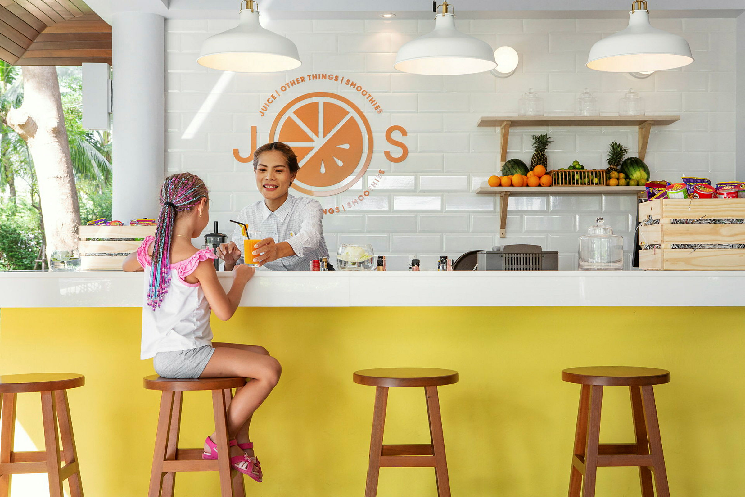 En jente sitter ved en juicebar med fersk frukt og snacks på hyllen. (AI-generert tekst)