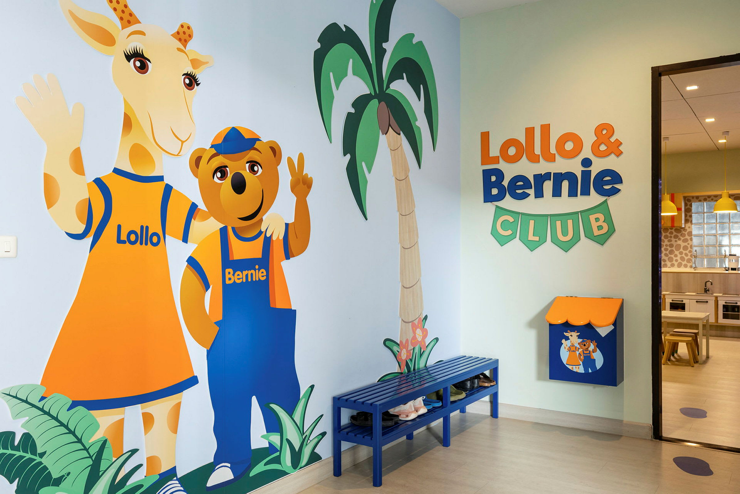 En fargerik veggmaleri av figurene Lollo og Bernie står ved en vegg i en barneklubb. Rommet har også en blå benk og skilt. (AI-generert tekst)