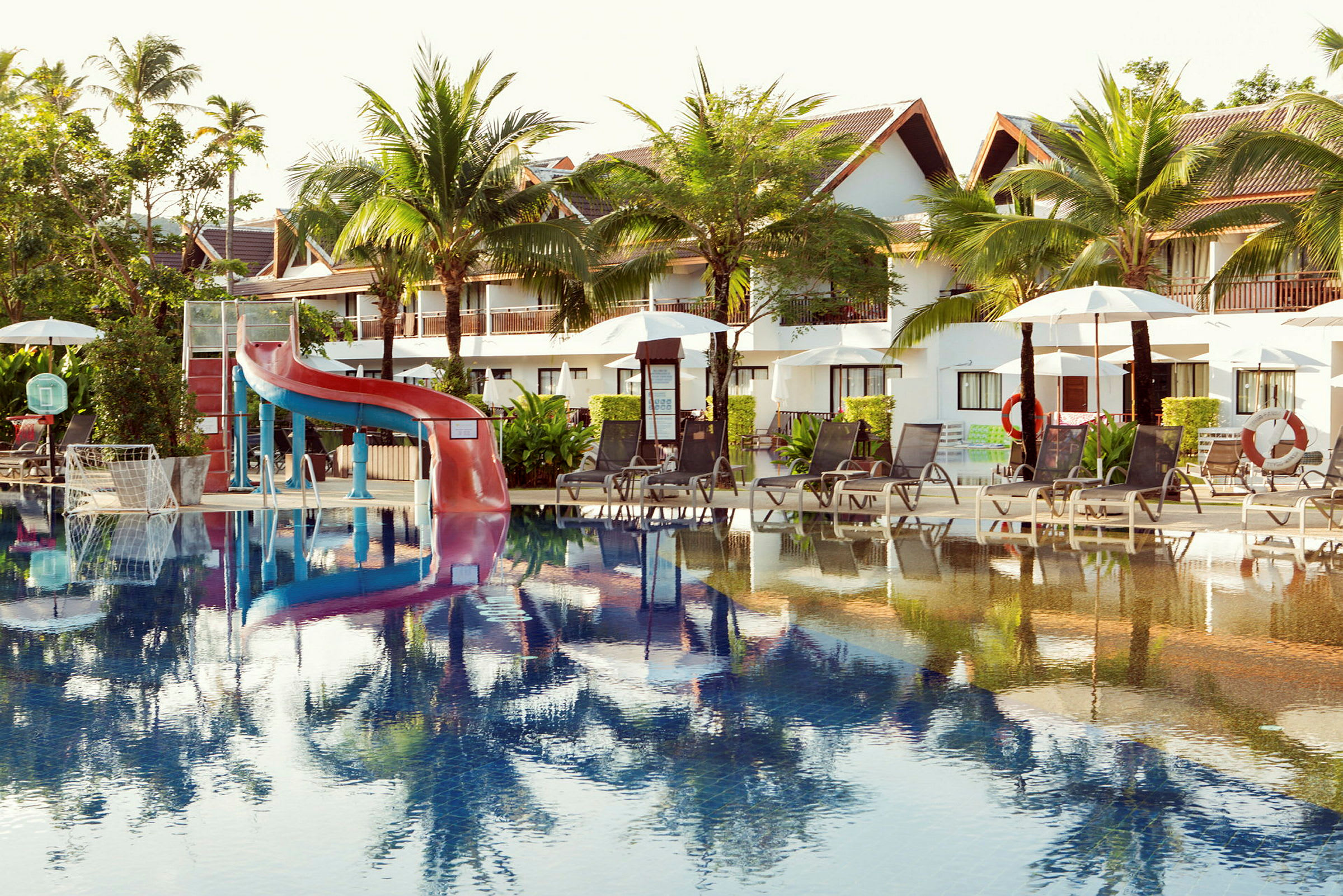 Bilde av et utendørsbasseng ved en resort med solsenger, parasoller og en vannsklie. (AI-generert tekst)