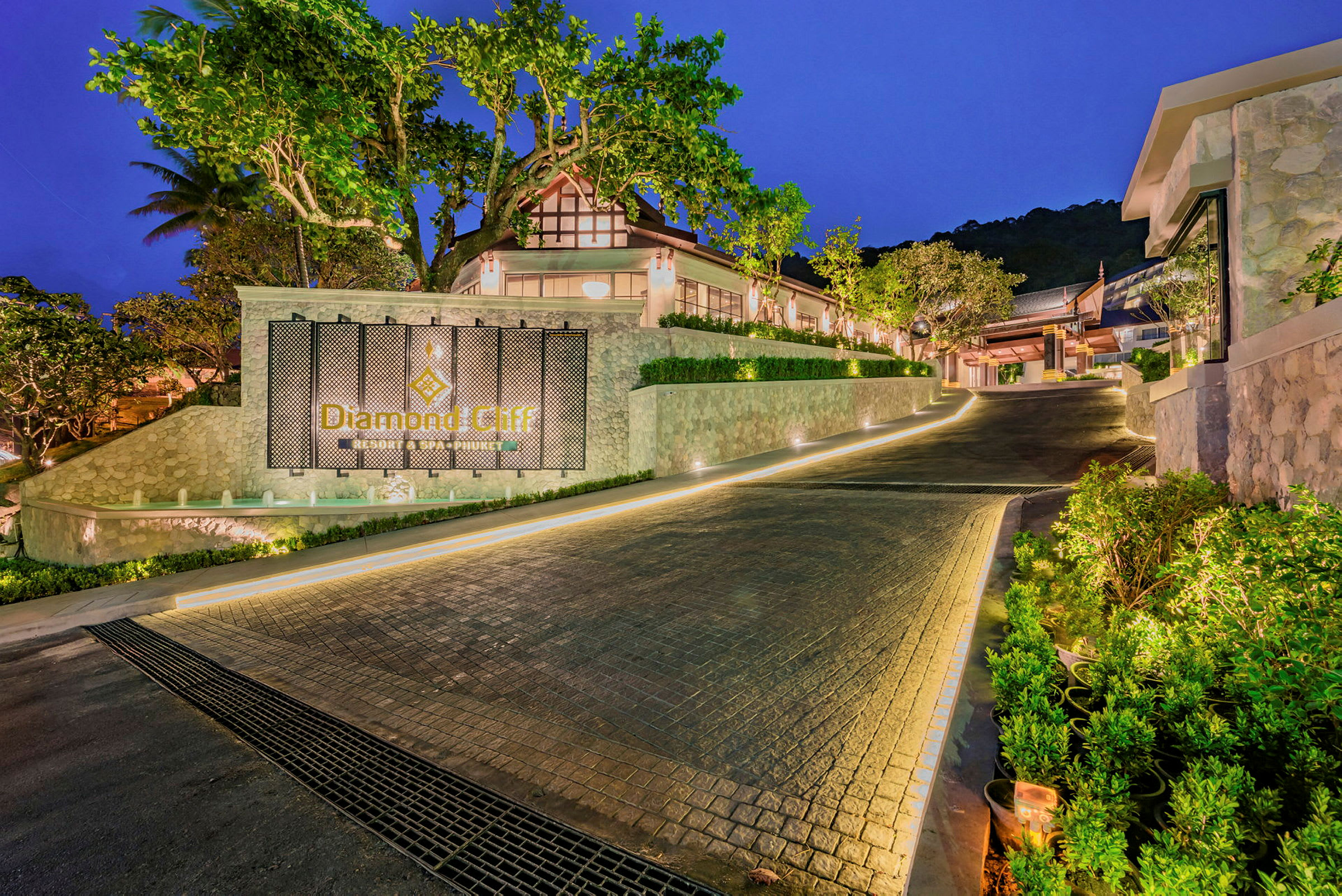 Inngang til Diamond Cliff Resort, omgitt av planter og opplyst svingete vei. (AI-generert tekst)