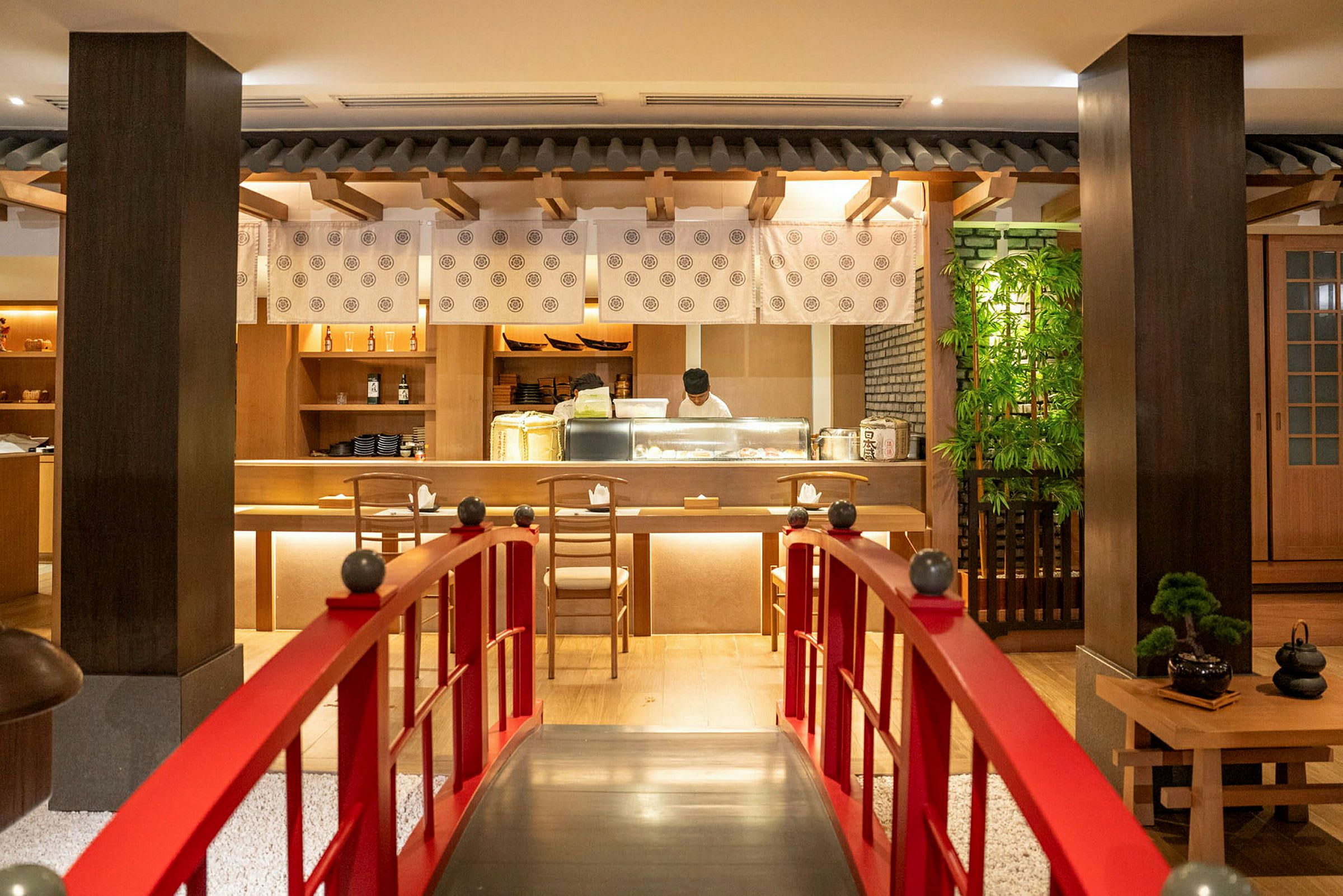 En restaurantinnredning med fokus på japansk stil, en rød bro leder frem til en bar der en kokk arbeider. (AI-generert tekst)