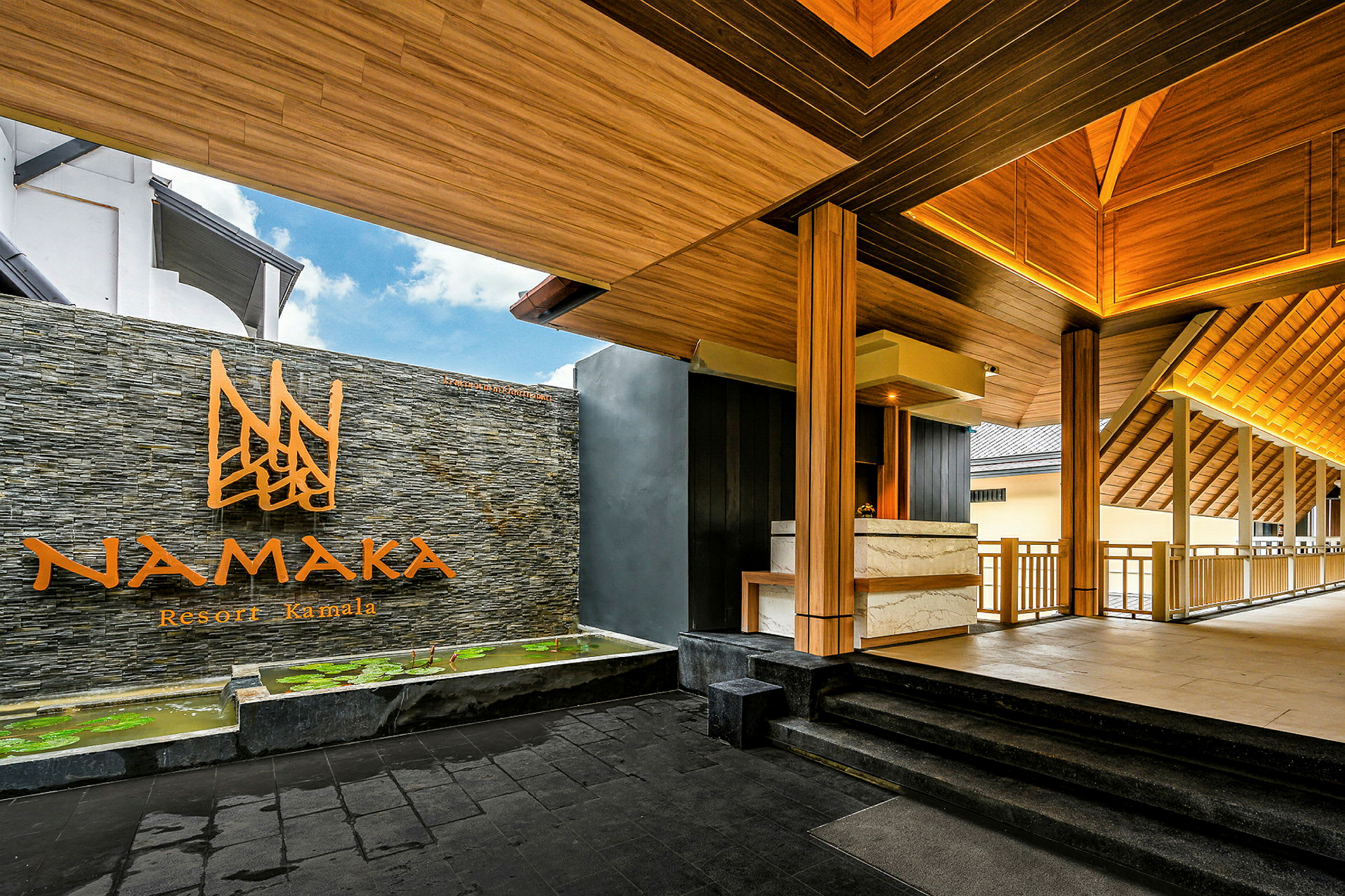 Inngang til Namaka Resort Kamala med tretak og steinmur. (AI-generert tekst)