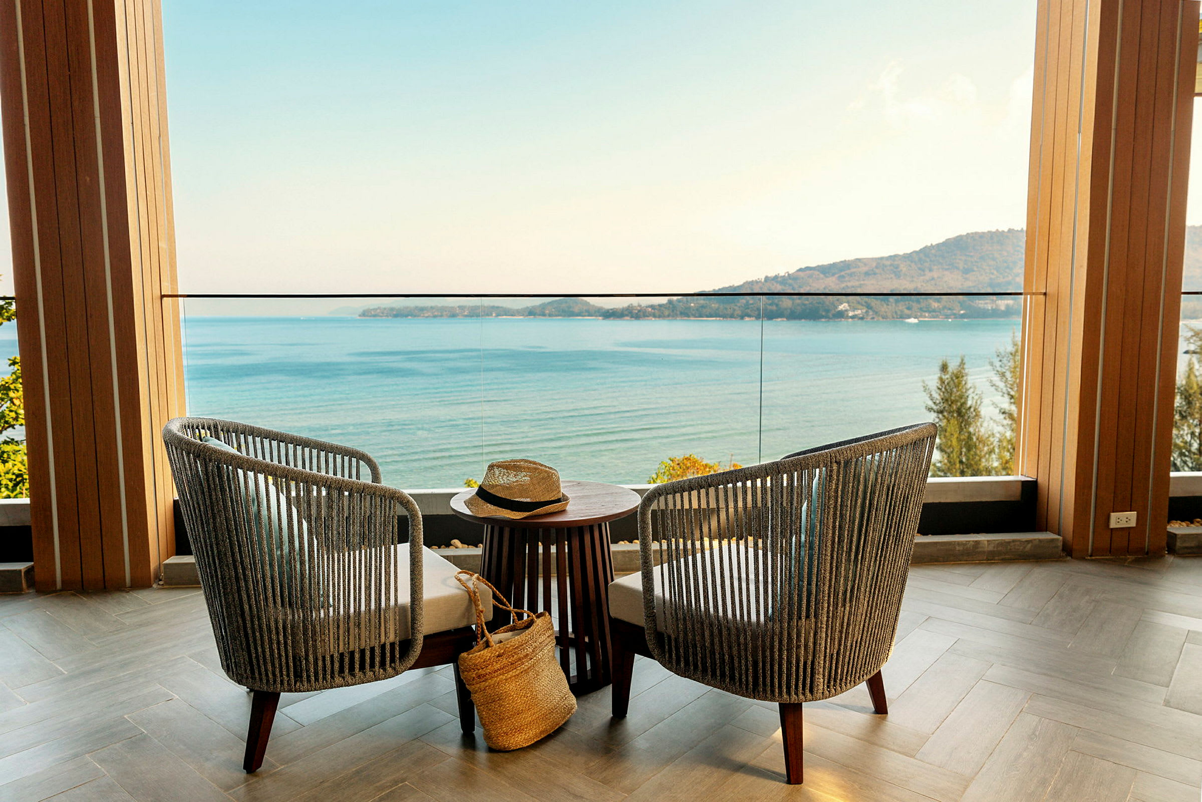 To stoler og et bord står på en terrasse med utsikt over havet og en fjellkyst. (AI-generert tekst)