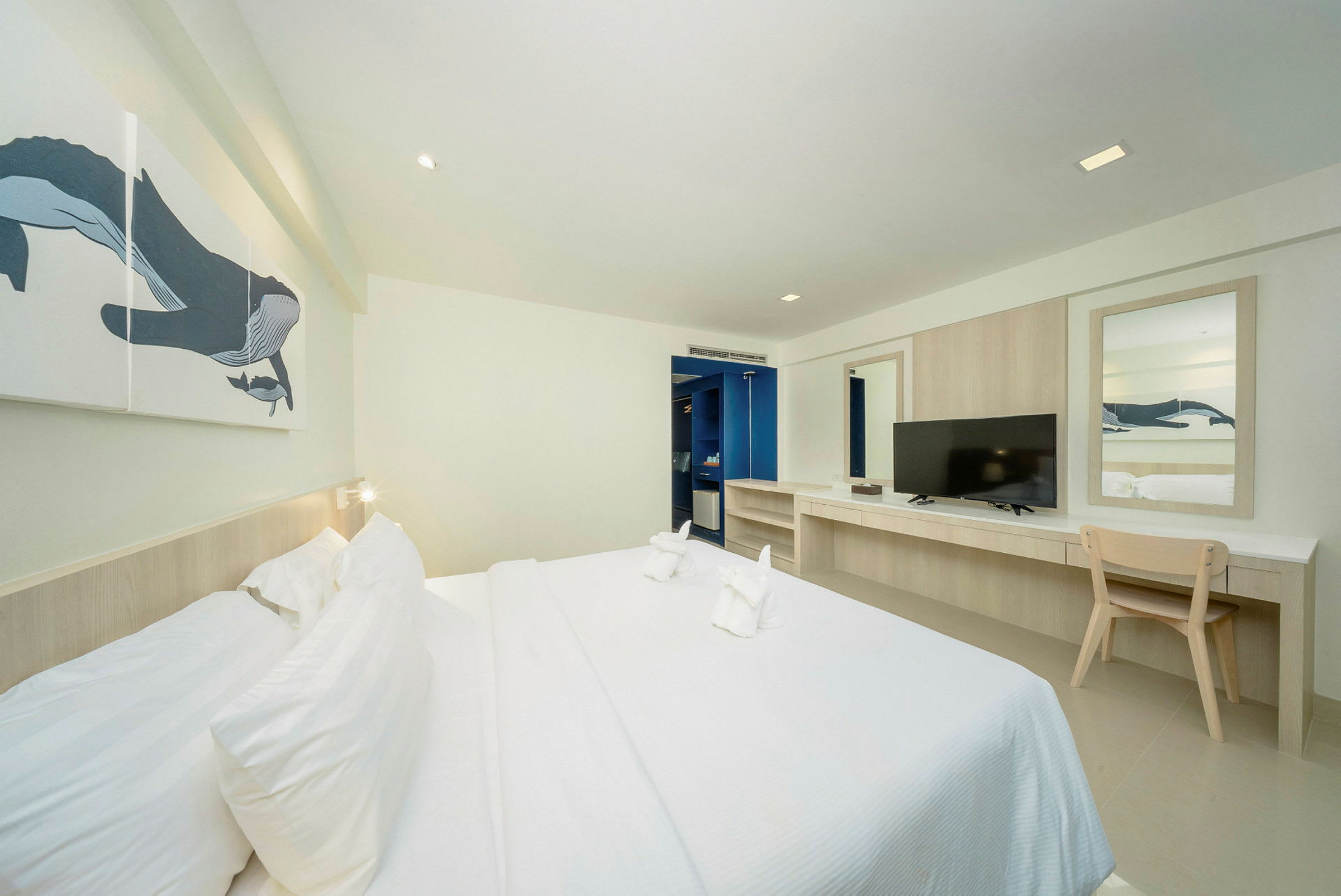 Et hotellrom med en dobbeltseng, skrivebord, TV og veggkunst. (AI-generert tekst)