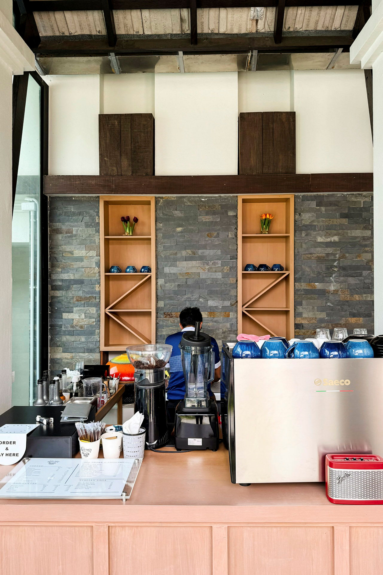 En kafédisk med espressomaskin og kaffekopper, en person jobber ved den. (AI-generert tekst)