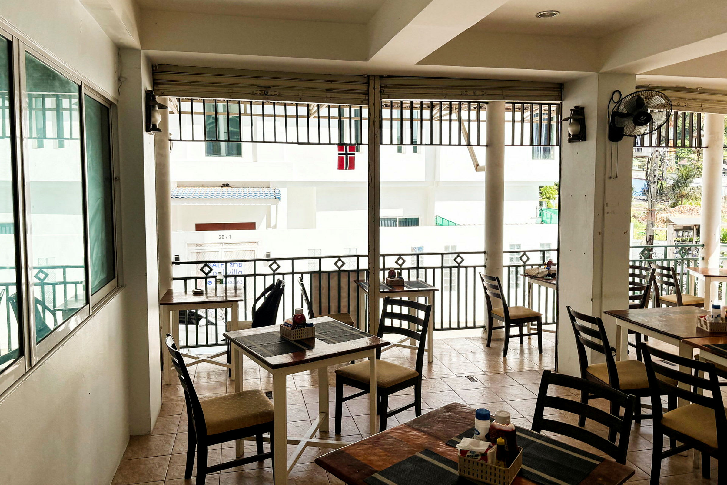En utendørs kafé eller restaurant med bord og stoler, samt utsikt over en bygning. (AI-generert tekst)