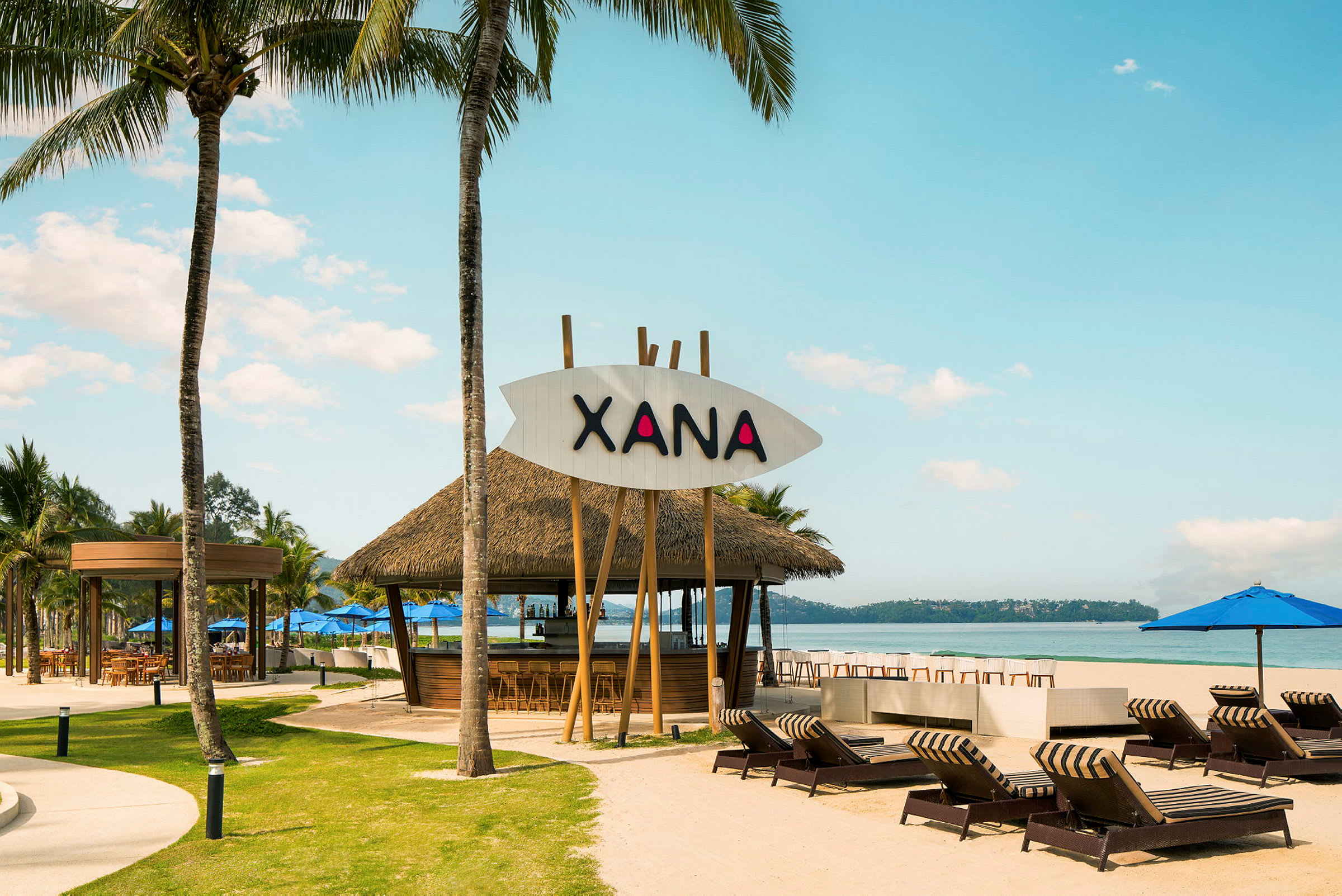 En strandmiljø med solsenger, parasoller og en strandrestaurant med navnet Xana. (AI-generert tekst)