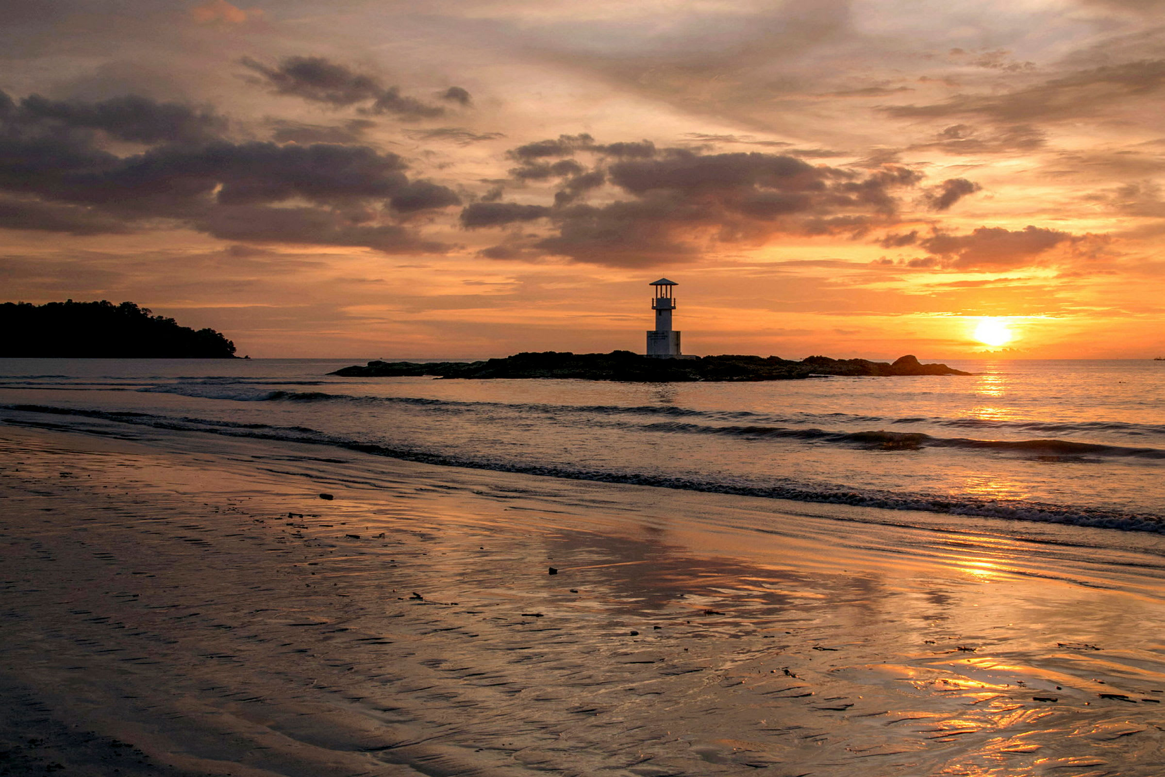 Solnedgang ved en strand, med et fyrtårn på et steinete nes og himmelen farget i oransje og rosa nyanser. (AI-generert tekst)