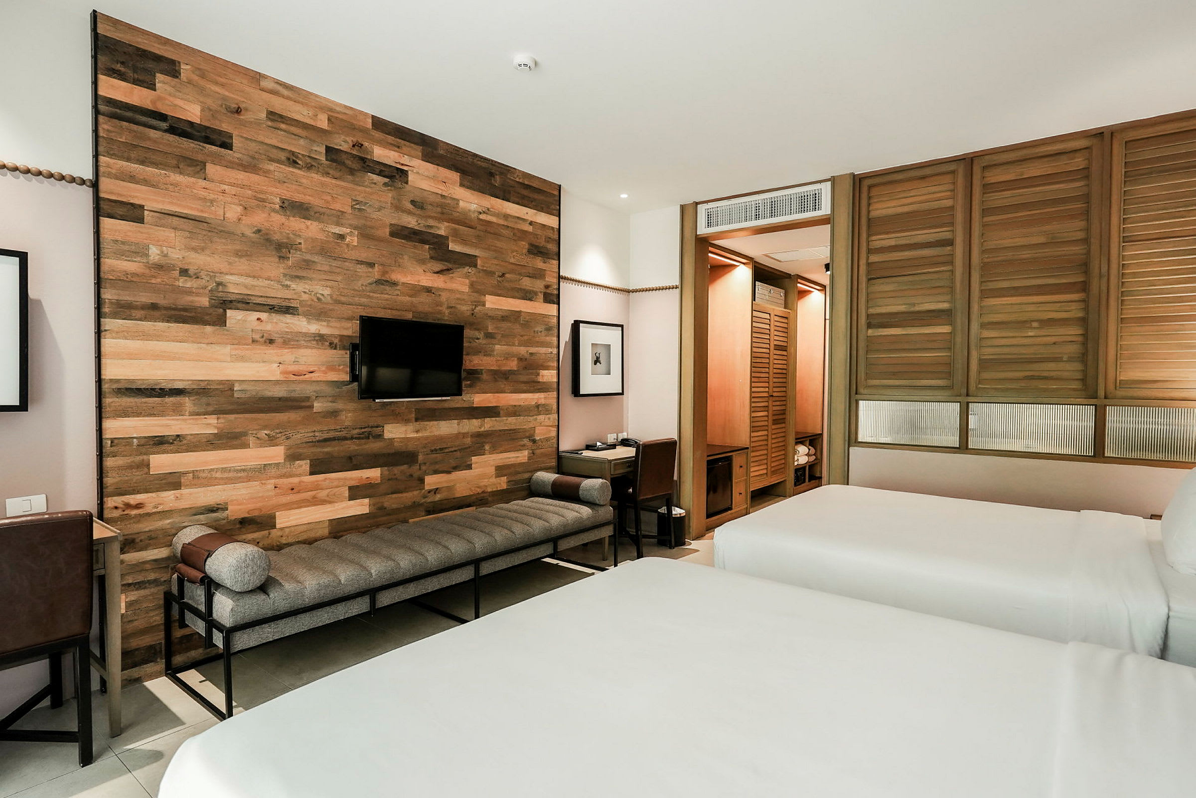 Moderne innredet hotellrom med trepanelvegg, to senger, en benk og et skrivebord. (AI-generert tekst)
