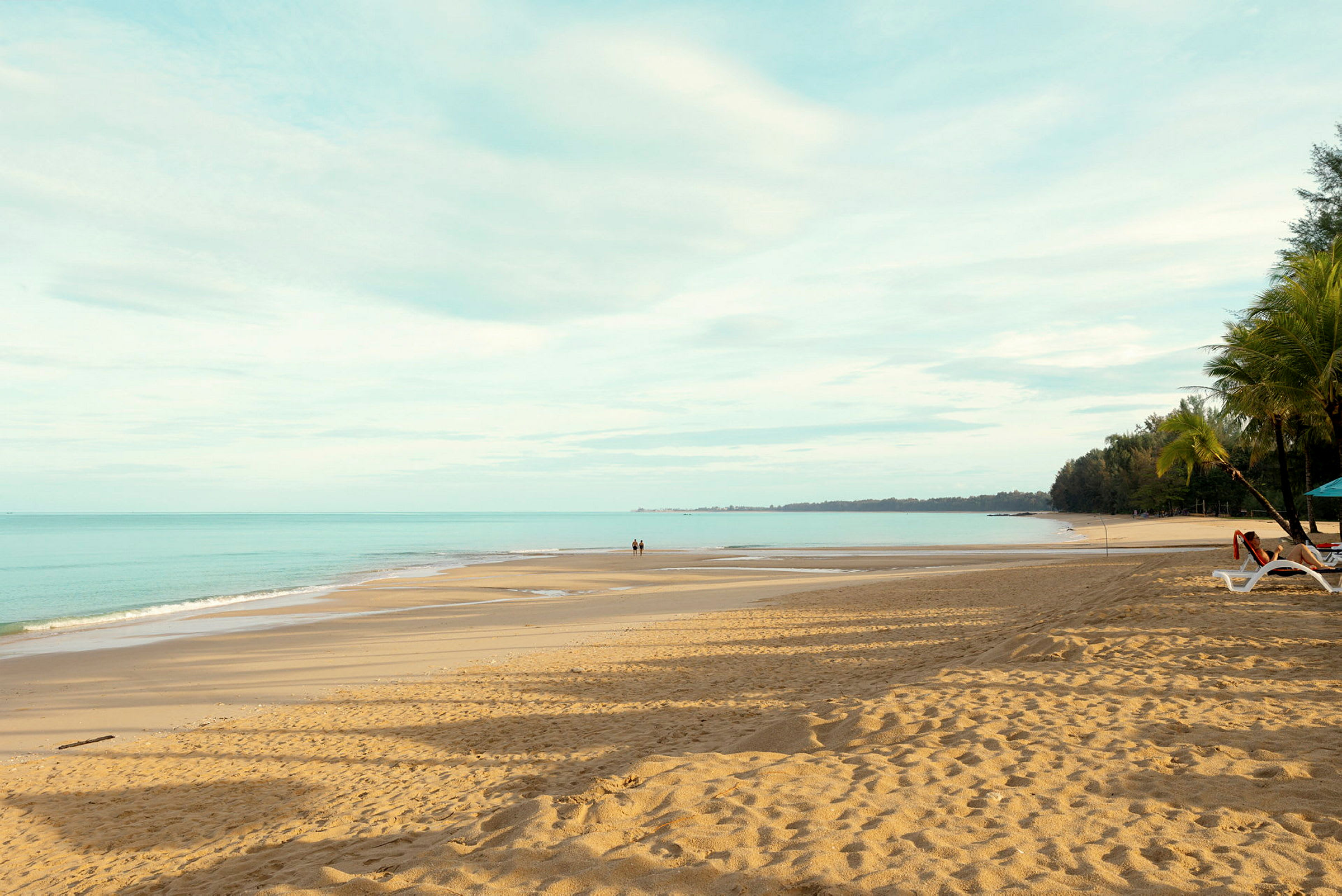 En sandstrand med utsikt over havet, to personer går på stranden. (AI-generert tekst)