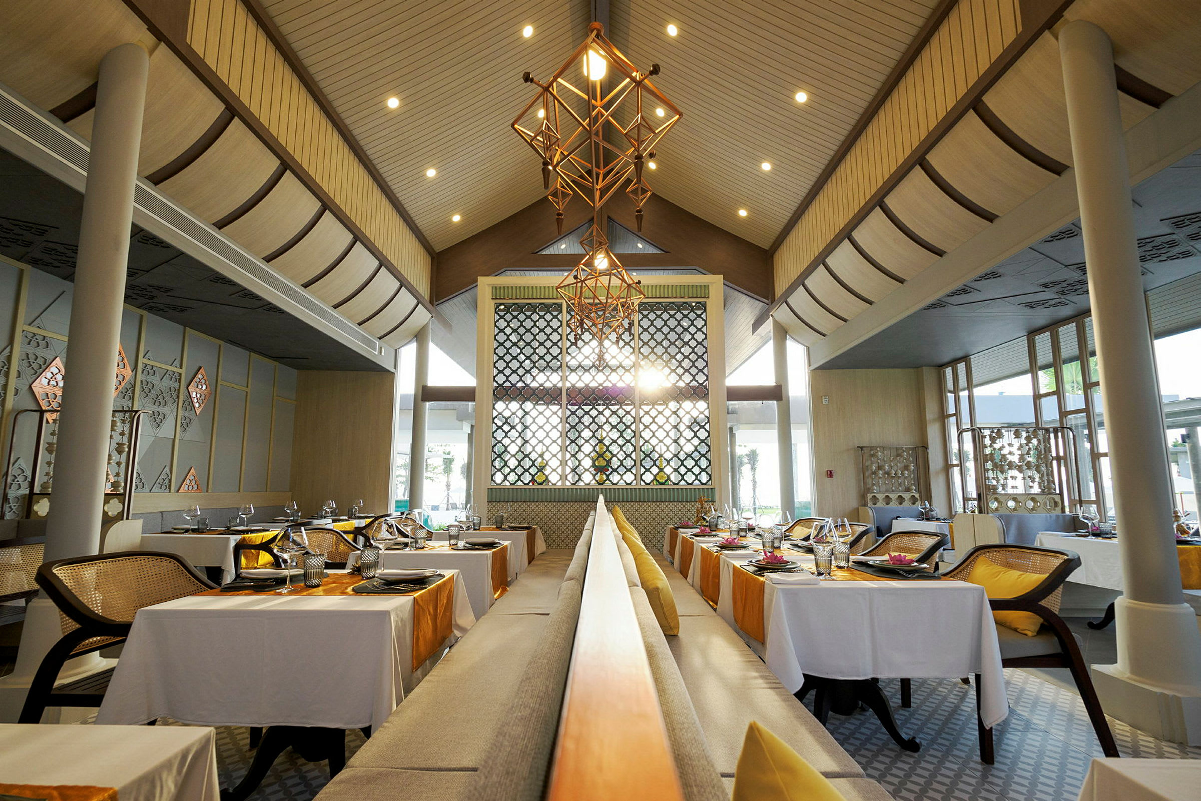 Bilde av en elegant restaurant med bord dekket for middag, dekorert med hvite duker og oransje løpere, samt moderne takbelysning. (AI-generert tekst)
