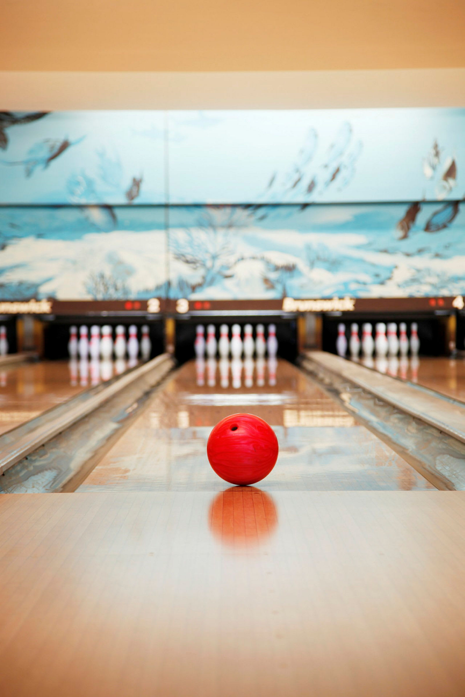 En rød bowlingkule ligger på en bowlingbane, med kjegler i bakgrunnen. (AI-generert tekst)