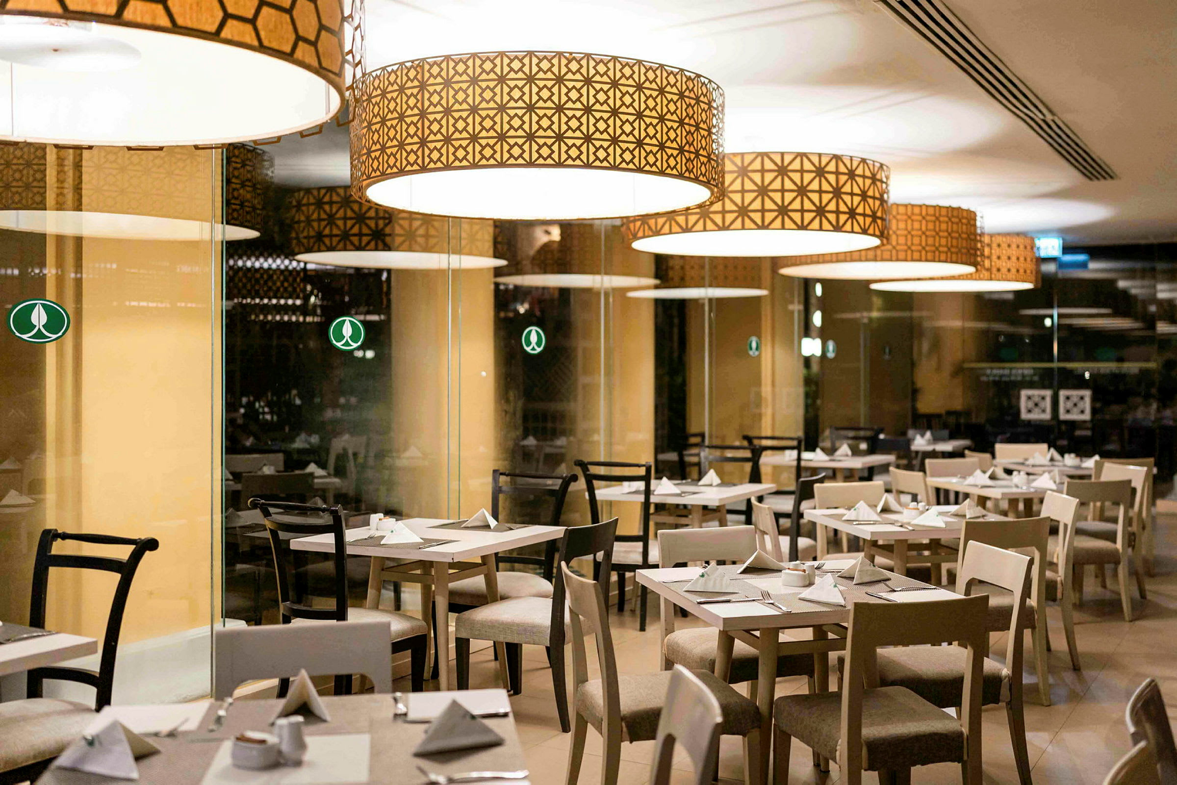 Bilde av en restaurant med flere dekkede bord og stoler under store dekorative lamper. (AI-generert tekst)