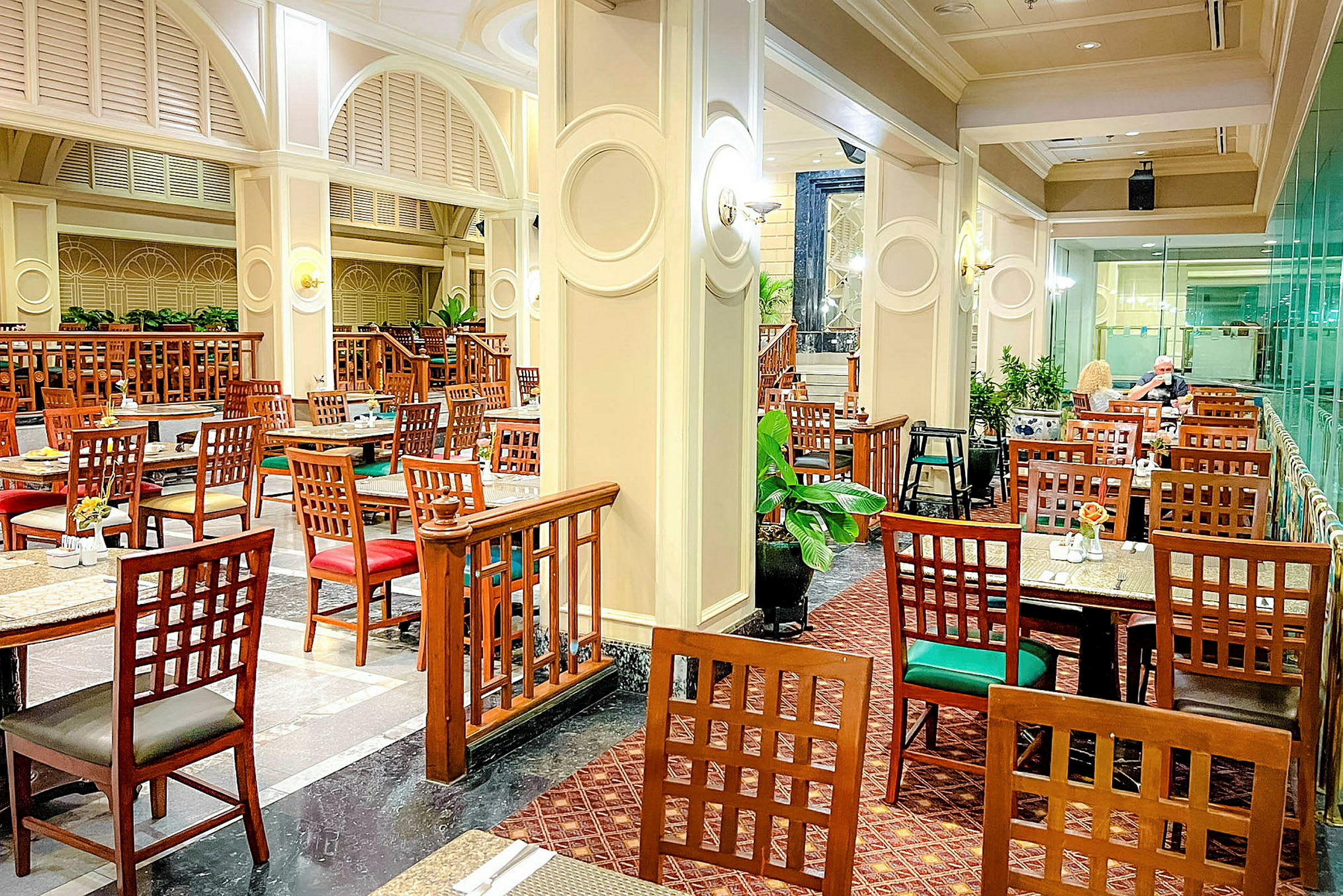 Restaurant med bord og stoler i tre, interiør med arkitektoniske detaljer og planter. (AI-generert tekst)