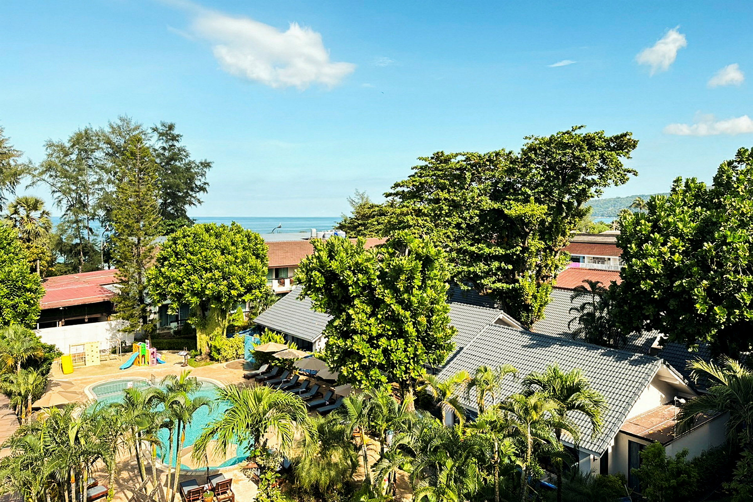 Utsikt over hotellområde med basseng og frodig vegetasjon, i bakgrunnen sees havet. (AI-generert tekst)