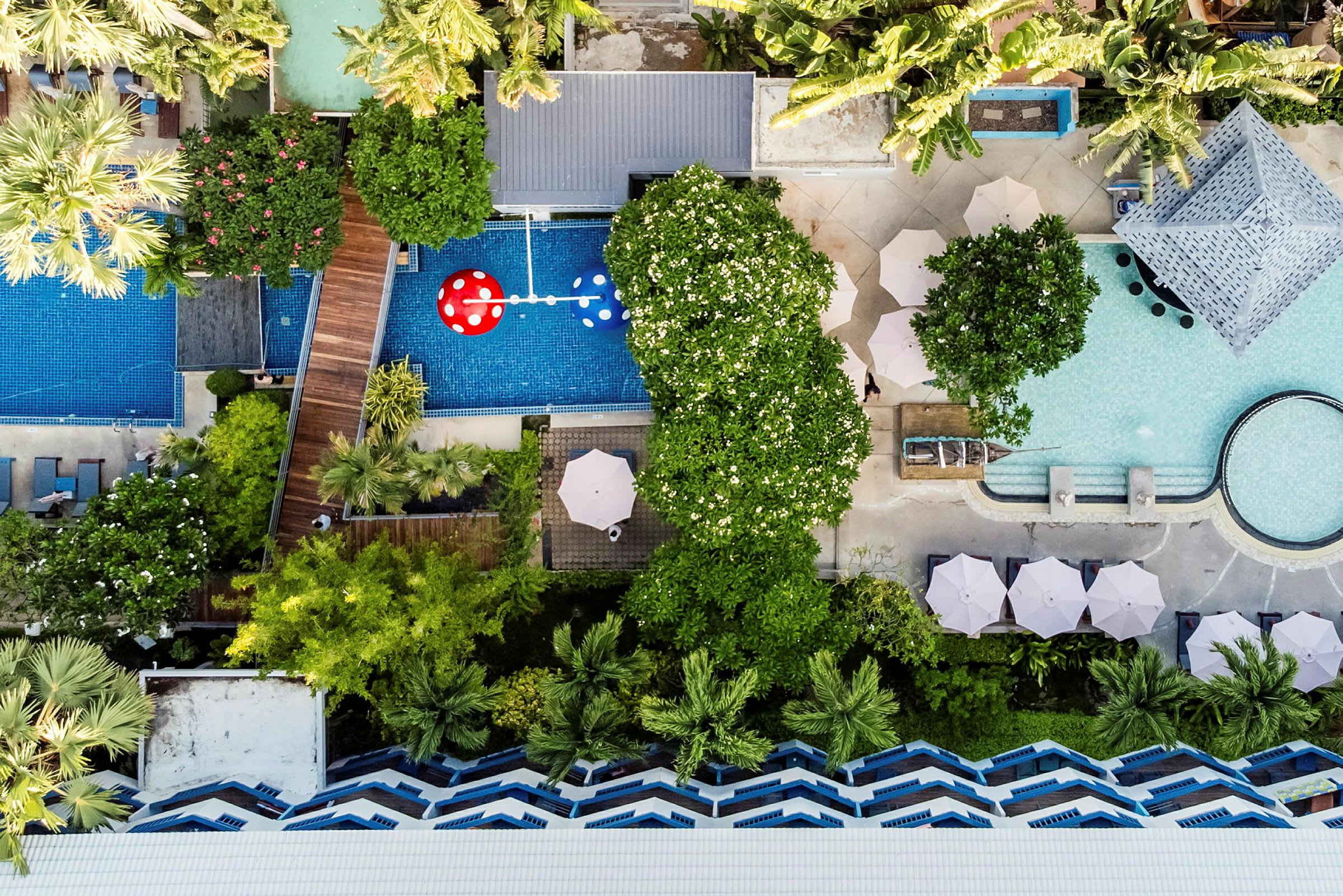 Flyfoto av et hotellområde med bassenger, grøntområder og parasoller. (AI-generert tekst)