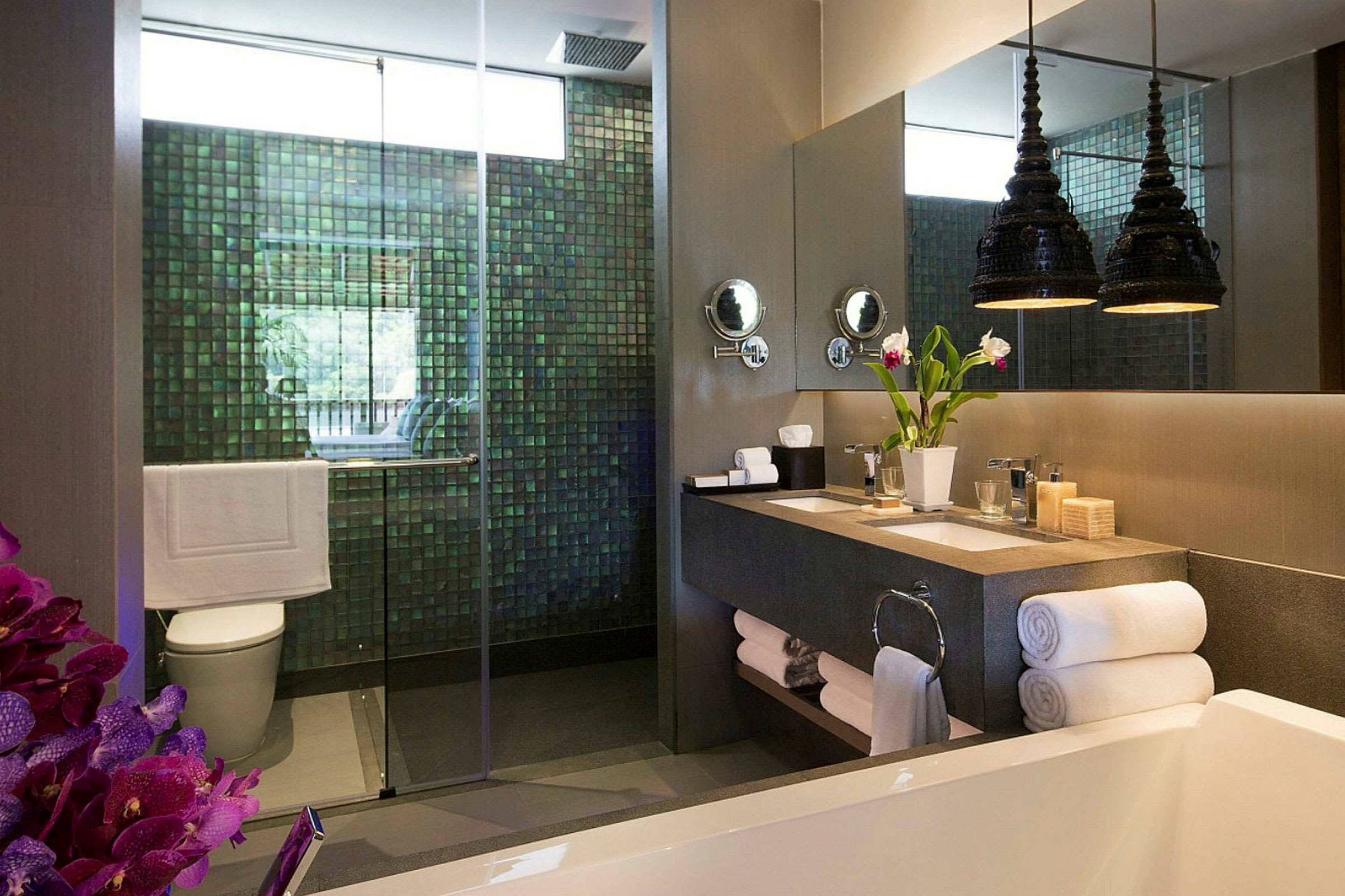 Et moderne bad med en dusj med glassdør, en doble servant med speil over, en dekorativ vase med blomster og håndklær pent stablet. (AI-generert tekst)