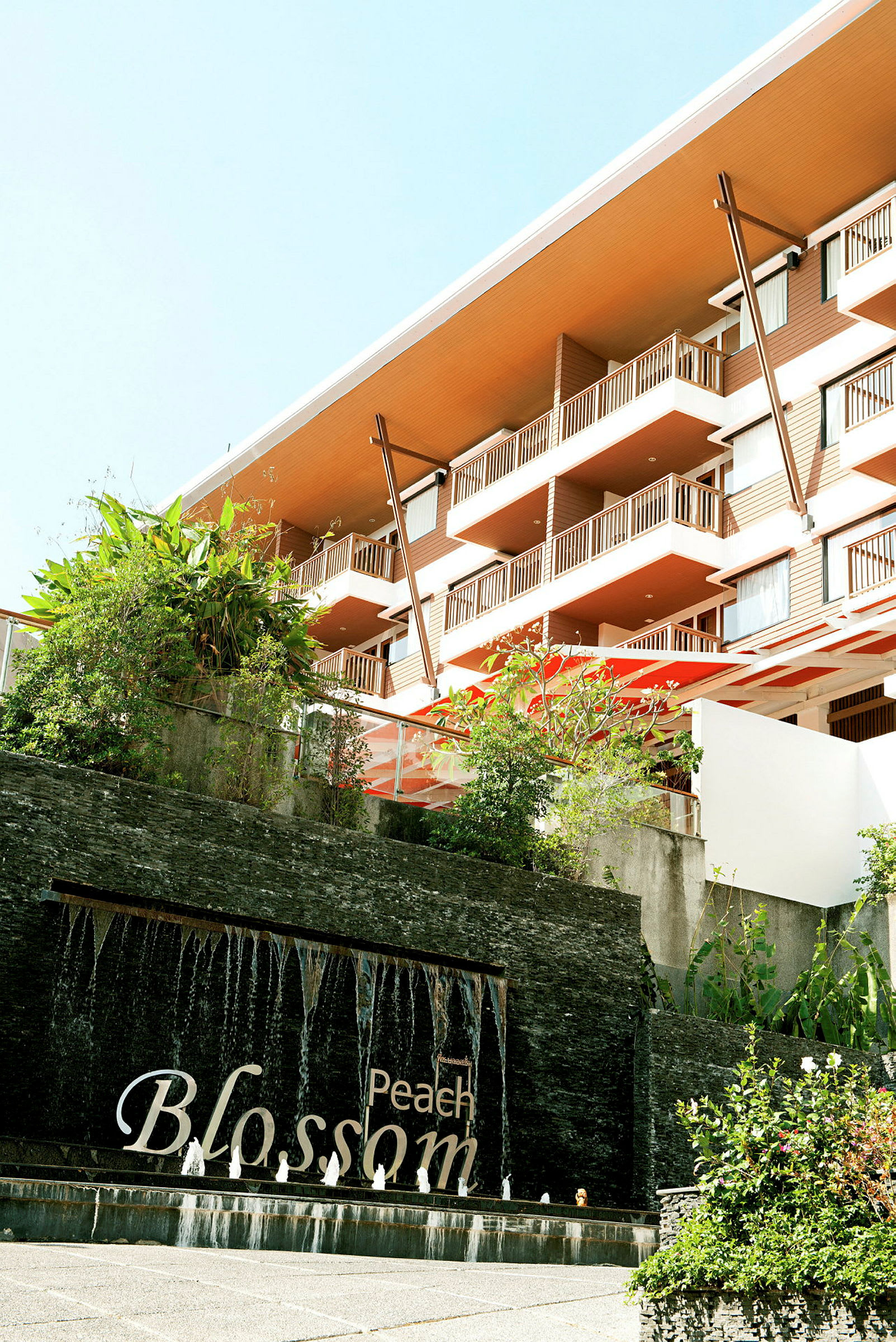 Et hotell med moderne balkonger, grøntområde og en fontene med teksten "Peach Blossom". (AI-generert tekst)