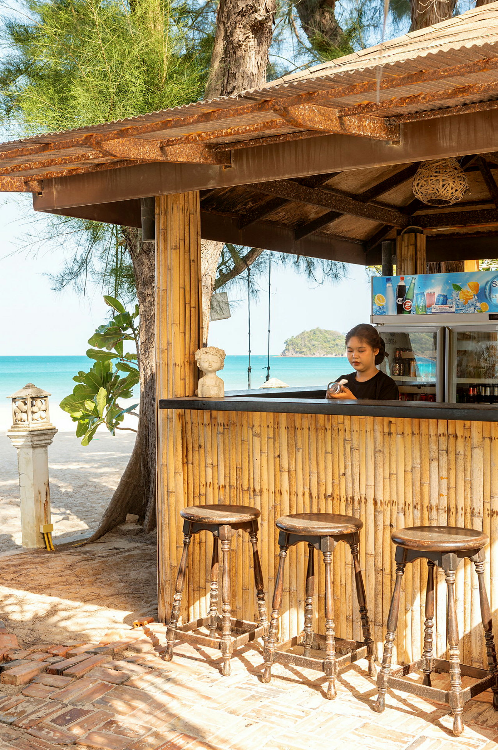 En bar med bambusvegger, trebarkrakker og strand i bakgrunnen. (AI-generert tekst)