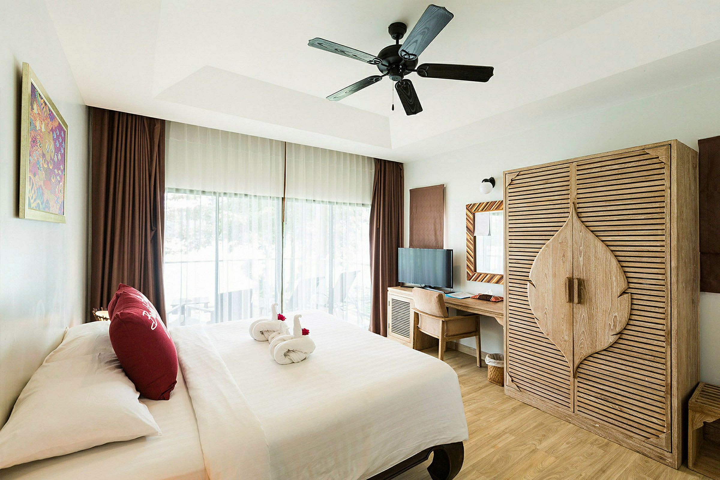 Et hotellrom med en dobbeltseng, et garderobeskap i tre, et skrivebord med stol og en takvifte. Et vindu med gardiner viser en balkong. (AI-generert tekst)